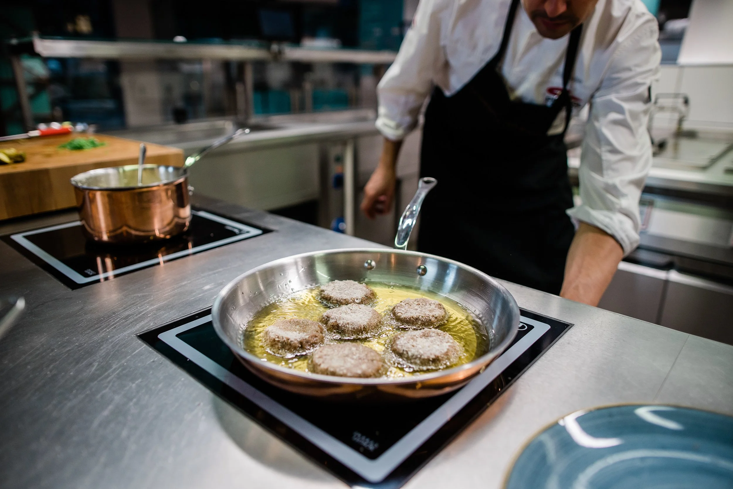 Chef frying breaded patties in a skillet on a stove in a commercial kitchen. Personal branding and fine dining restaurant photography in Zürich, Zug, Bern, Lucerne, Basel, St. Gallen and across Switzerland.