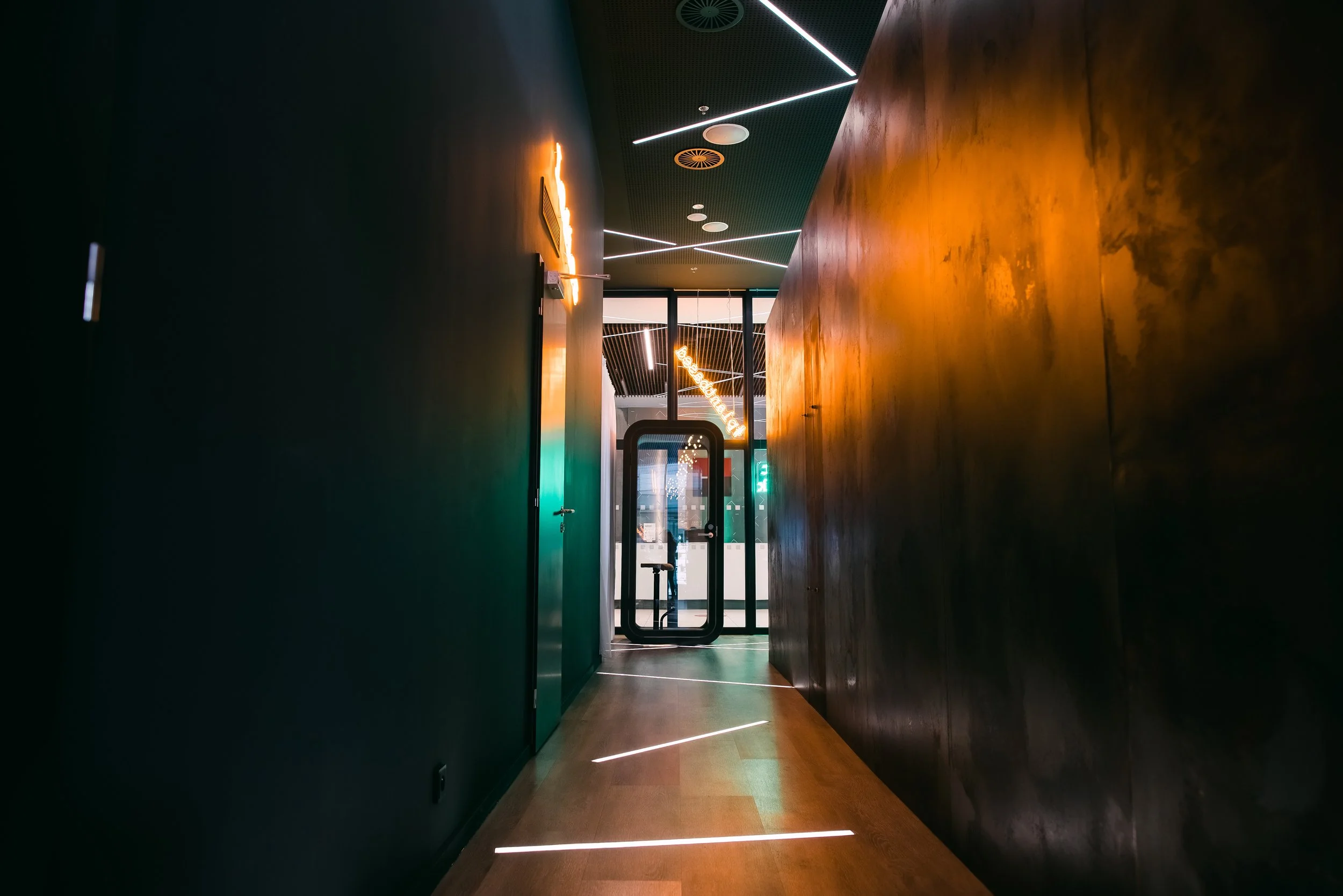 Modern hallway with black and brown walls, illuminated by sleek white and orange lighting, leading to glass doors at the end. Restaurant interior photography in Zürich, Zug, Bern, Lucerne, Basel, St. Gallen and across Switzerland.