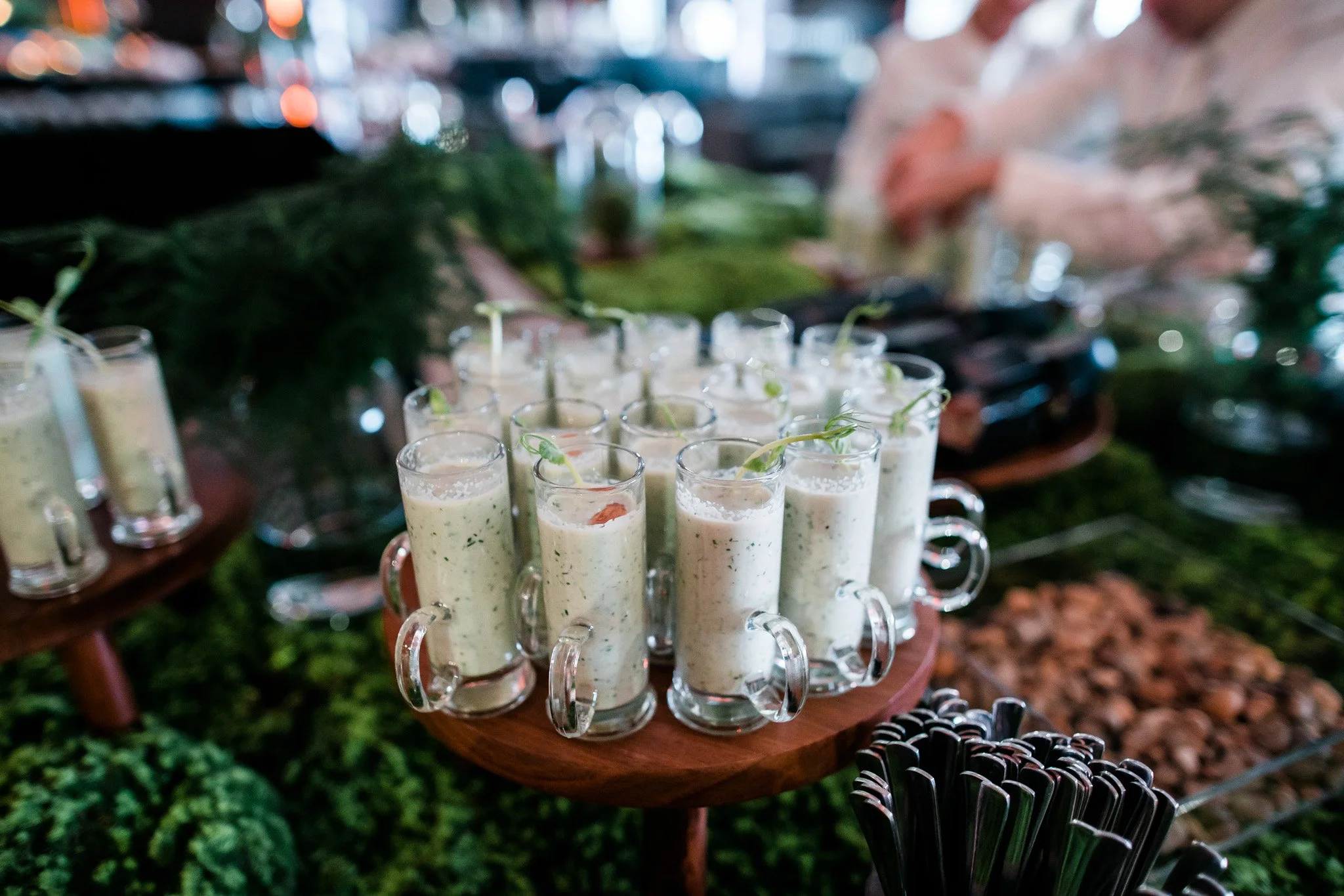 Multiple glasses of a creamy green dip garnished with herbs on a round wooden tray at a buffet. Catering and food photography in Zürich, Zug, Bern, Lucerne, Basel, St. Gallen and across Switzerland.