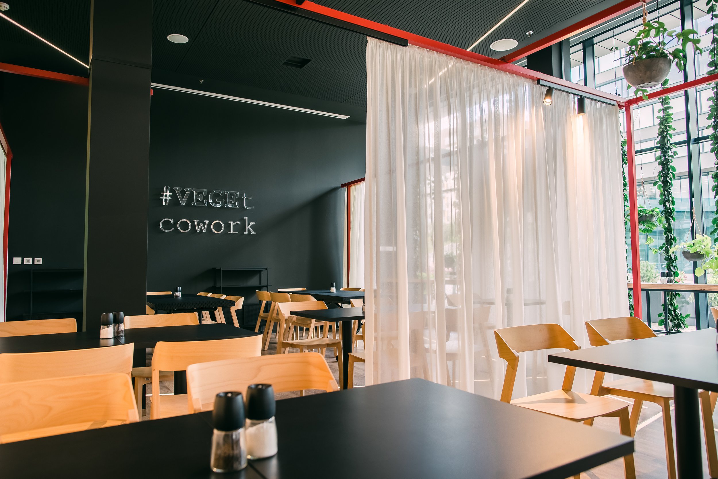 Modern coworking space with wooden chairs, black tables, white curtains, and a black wall with the logo illuminated in neon lights. Restaurant interior photography in Zürich, Zug, Bern, Lucerne, Basel, St. Gallen and across Switzerland.