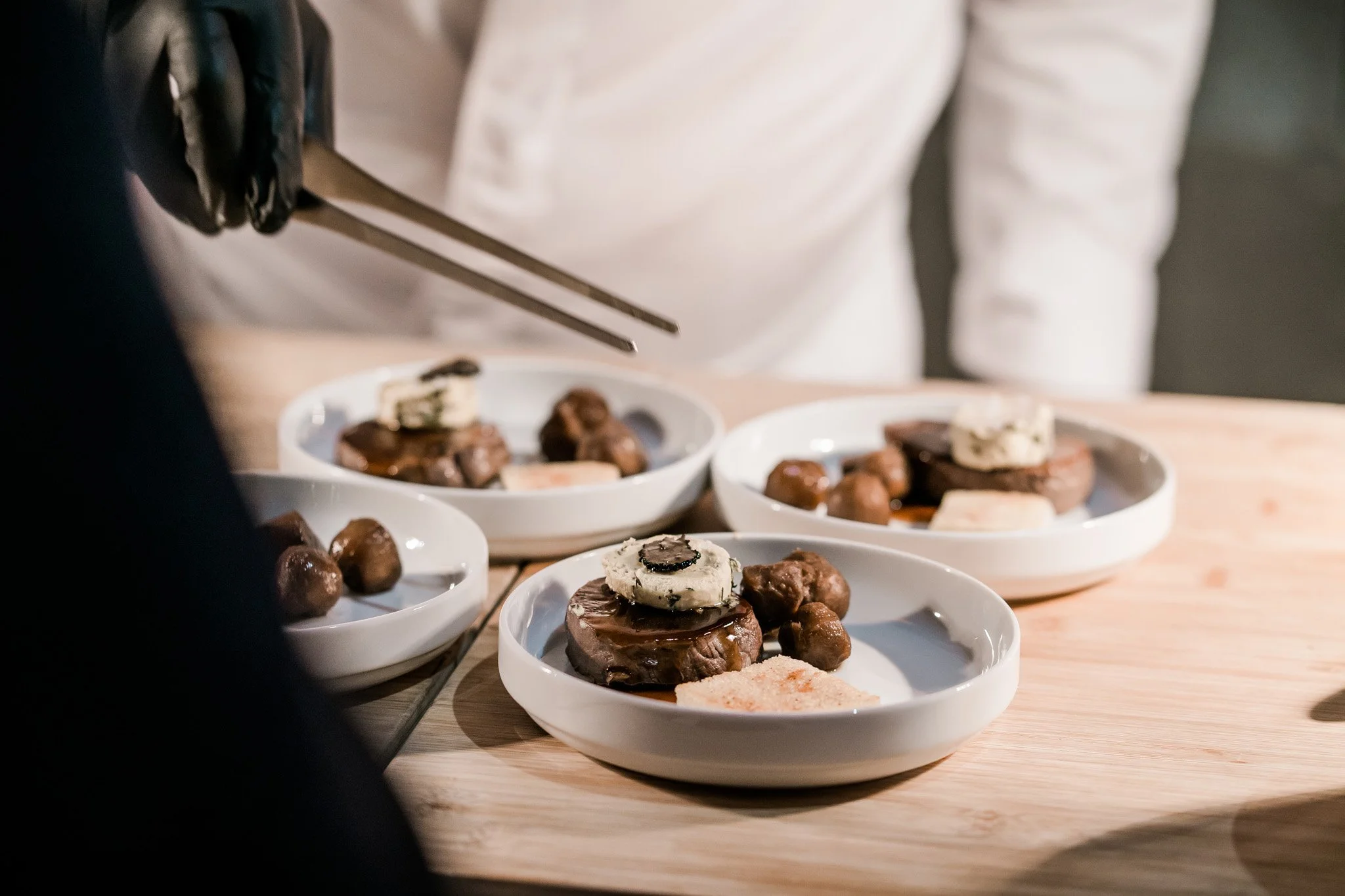 Chef preparing meat on white plates. Catering and food photography in Zürich, Zug, Bern, Lucerne, Basel, St. Gallen and across Switzerland.