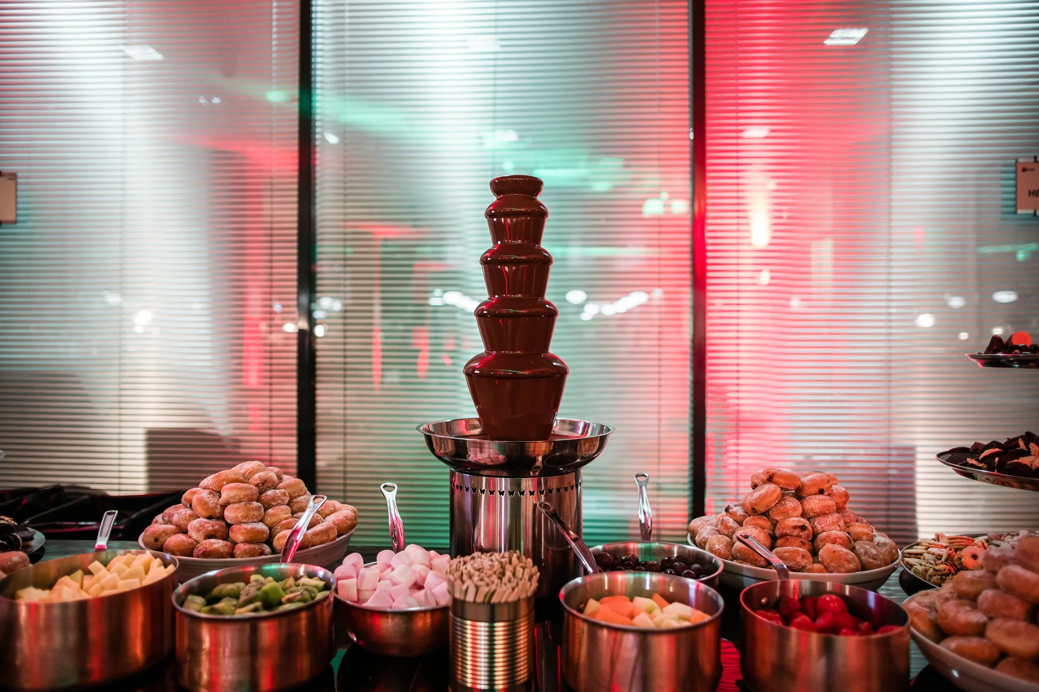 Chocolate fountain surrounded by bowls of candies and cookies at a dessert table. Catering and food photography in Zürich, Zug, Bern, Lucerne, Basel, St. Gallen and across Switzerland.