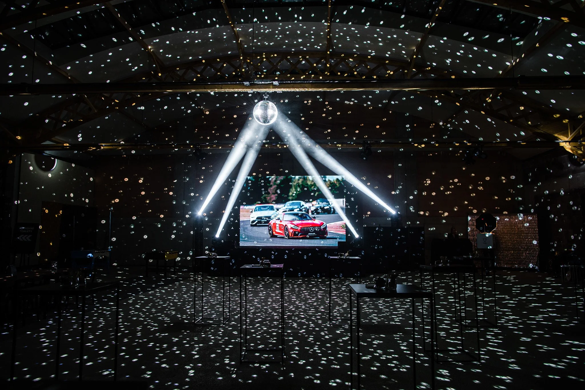 Indoor event with a large screen displaying sports cars, and a disco ball hanging from the ceiling, with light effects projected onto the walls and floor. Car event photography in Zürich, Zug, Bern, Lucerne, Basel, St. Gallen, Switzerland.