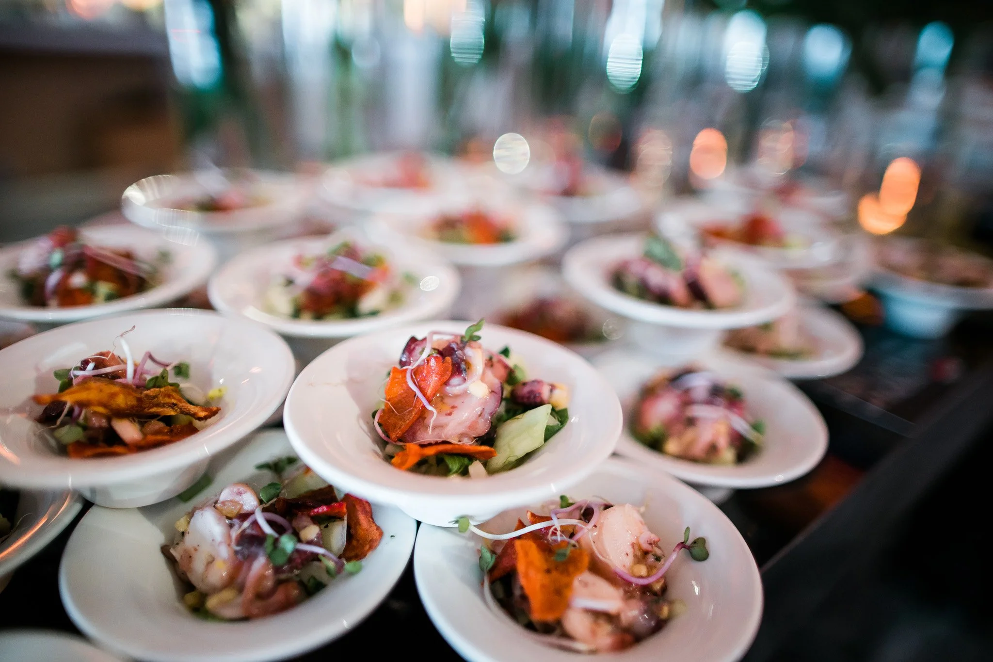 Multiple small white plates with colorful salads and garnishes on a table in a restaurant, blurred background. Catering and food photography in Zürich, Zug, Bern, Lucerne, Basel, St. Gallen and across Switzerland.