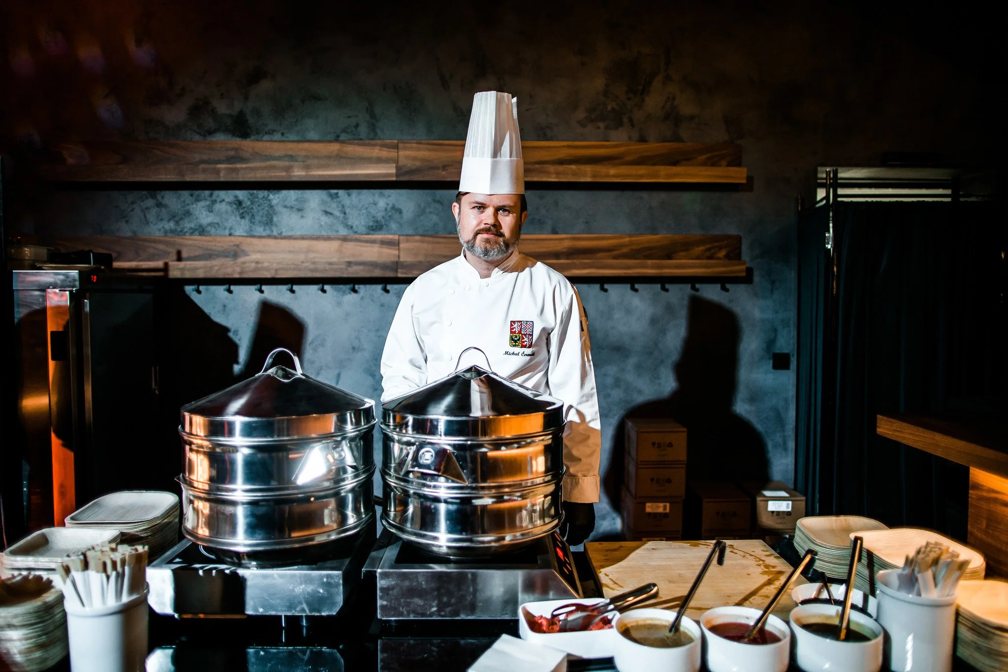 A chef standing behind a buffet station with chafing dishes, bowls of condiments, and stacks of plates in a restaurant setting. Catering and food photography in Zürich, Zug, Bern, Lucerne, Basel, St. Gallen and across Switzerland.
