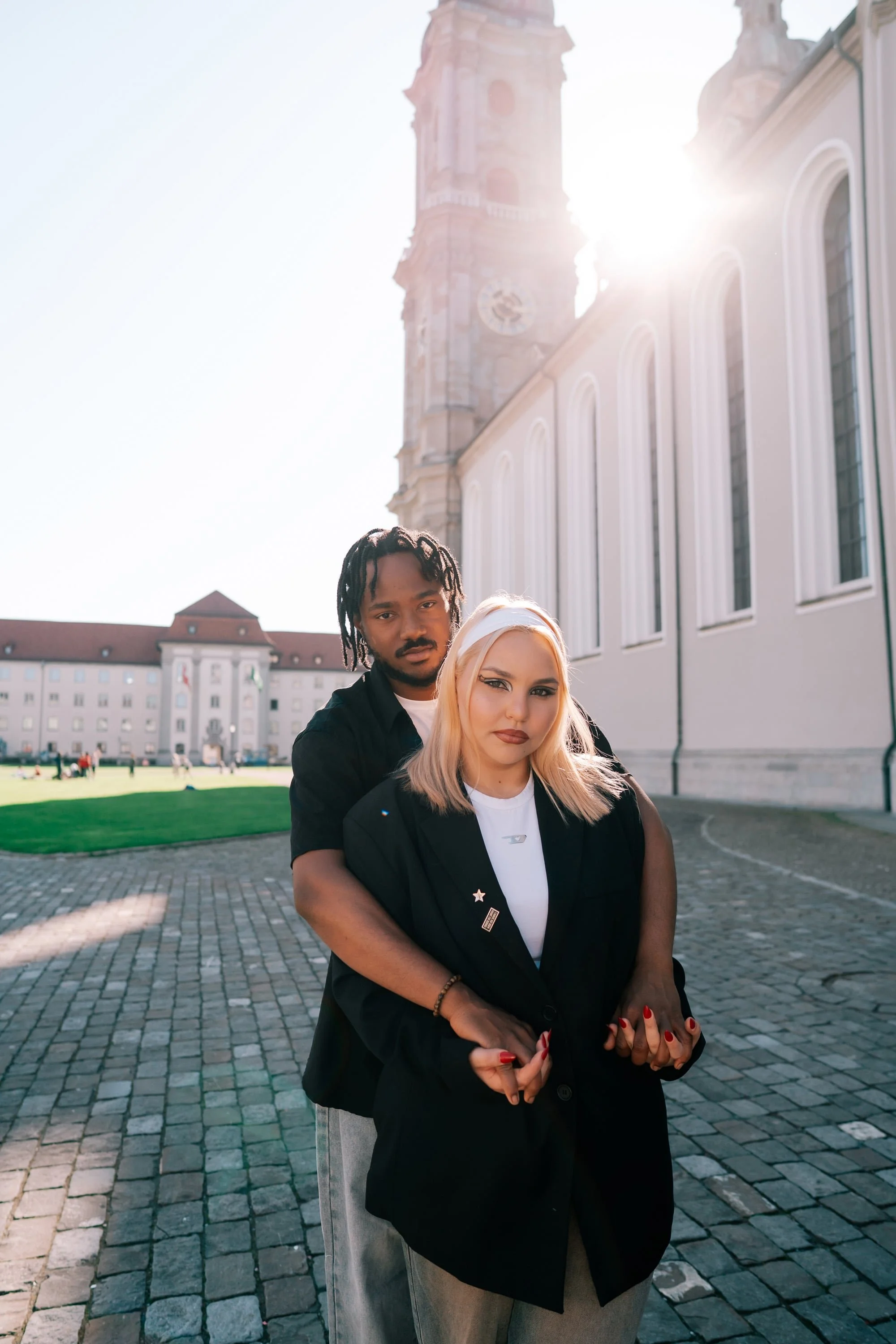 A man and a woman stand close together outside a historic building with a clock tower in St. Gallen Switzerland, with sunlight shining behind them.