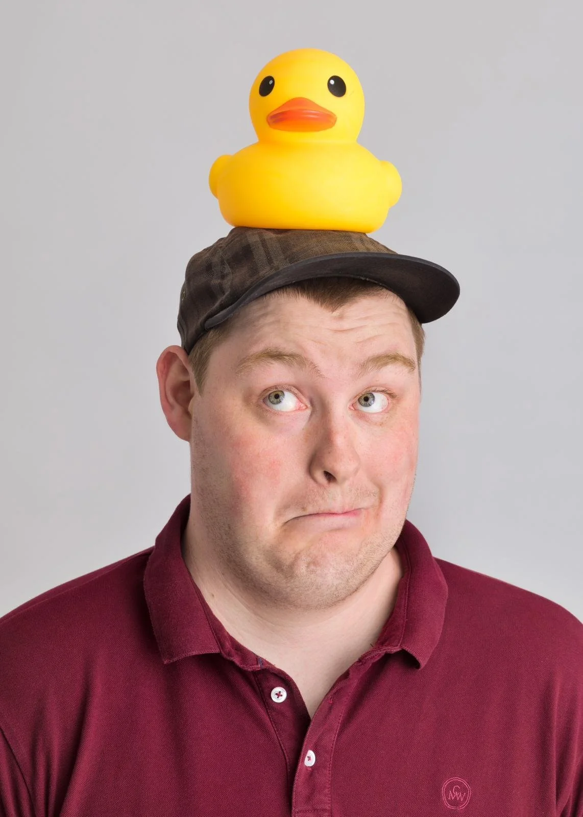 Man wearing a burgundy shirt with a toy rubber duck on his head.