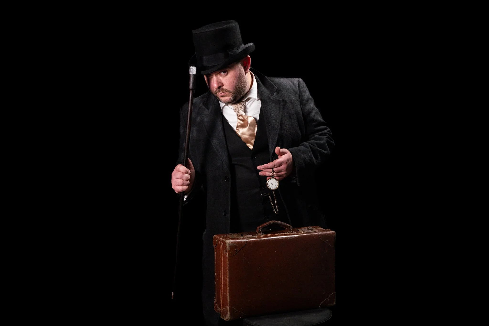 Man in a plaid suit holding a fishbowl with goldfish, pointing at his yellow tie, with a surprised expression