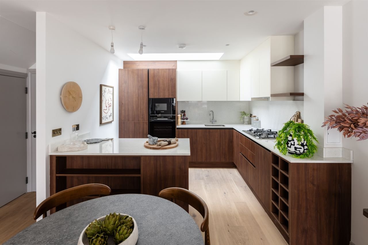 Modern kitchen with wooden cabinets, white countertops, a built-in oven, a gas stove, and a round dining table with a succulent centerpiece.