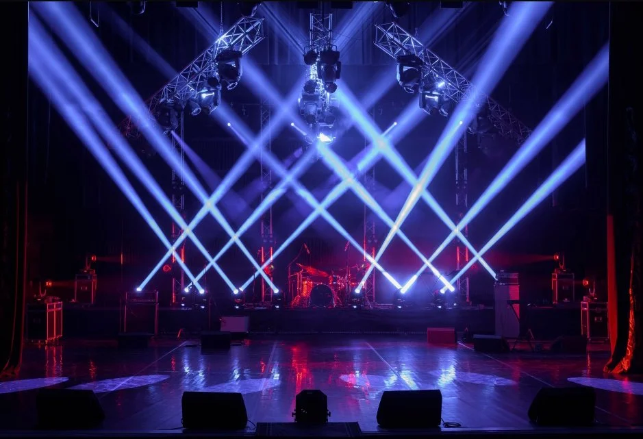 Empty concert stage with bright blue and white spotlights, musical instruments, and equipment