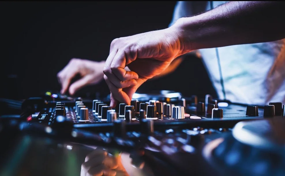 Close-up of a DJ adjusting controls on a professional mixing console in a dimly lit setting.