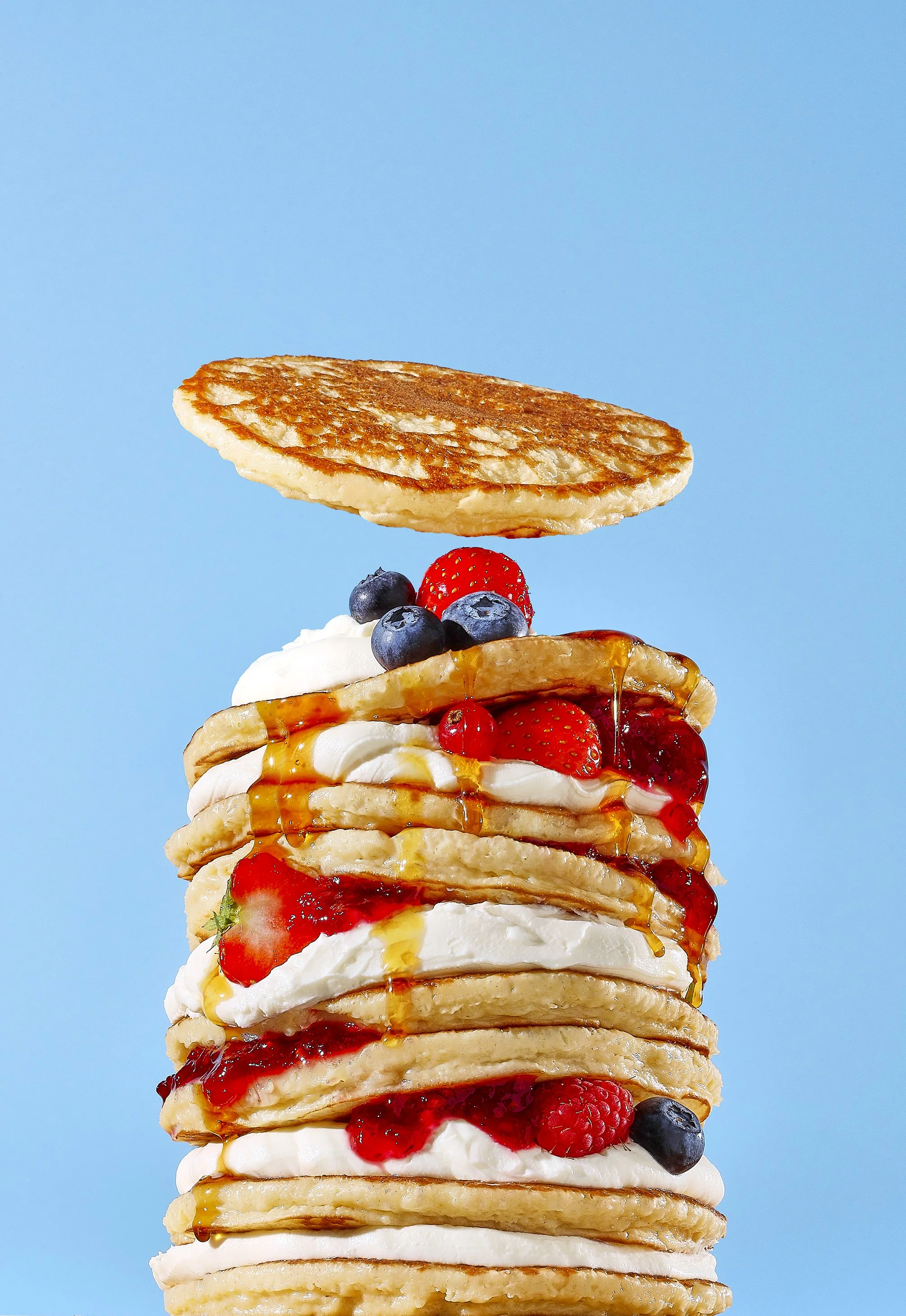 Sarah Ghijselinck, food and drink stylist, Gent, Stack of pancakes topped with assorted berries, whipped cream, syrup.