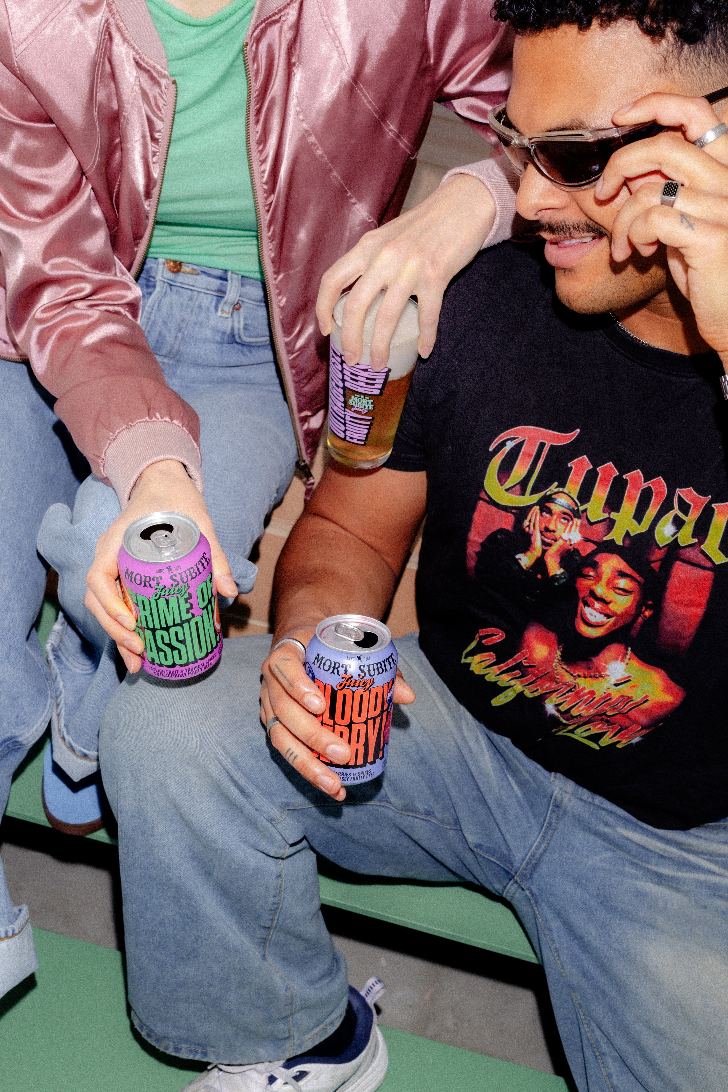 Drink styling and art direction Gent. Two people at a party holding colorful cans of Mort Subite and glasses of drinks, wearing casual clothing and sunglasses.