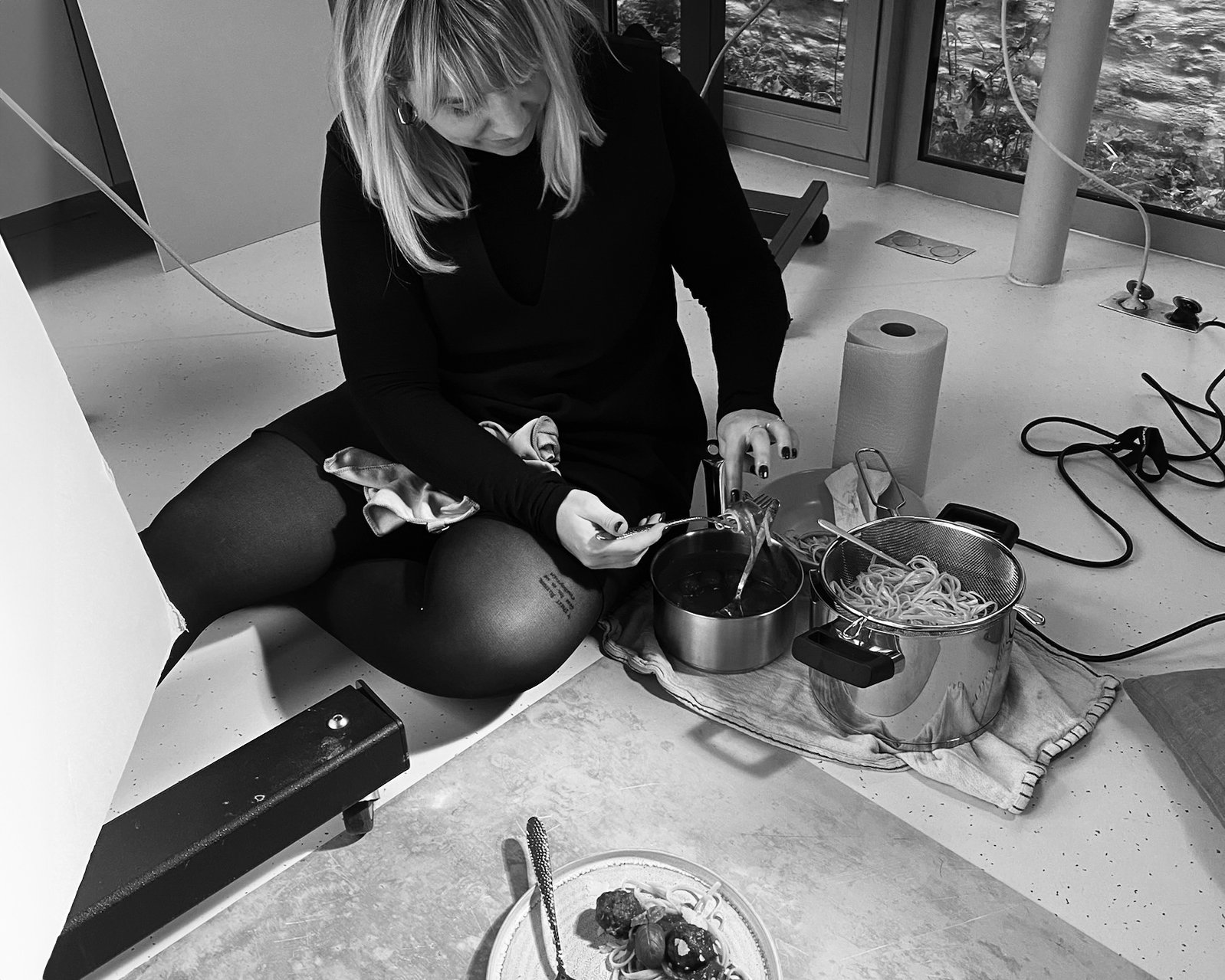 Sarah Ghijselinck food stylist, preparing food with spaghetti and sauce in a pot, surrounded by kitchen supplies including paper towels and utensils.