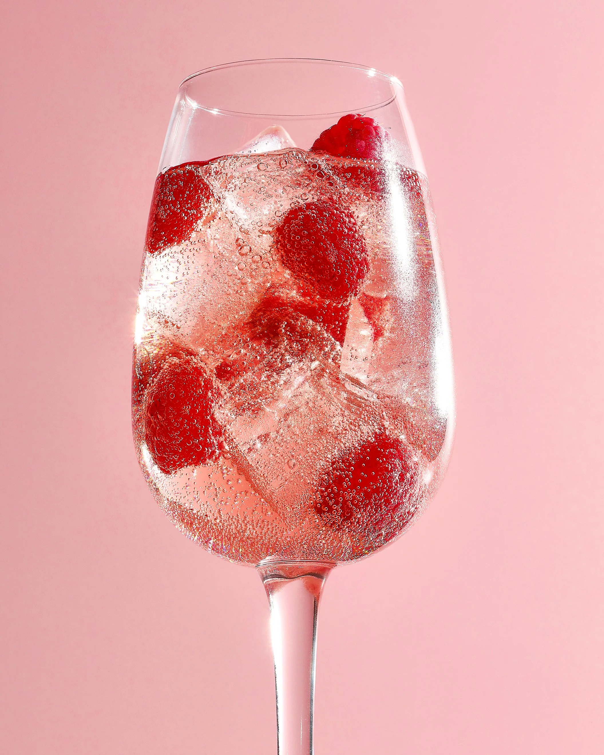 Sarah Ghijselinck, drink stylist, Gent, cocktail with bubbles rising in the clear sparkling water against a pink background.