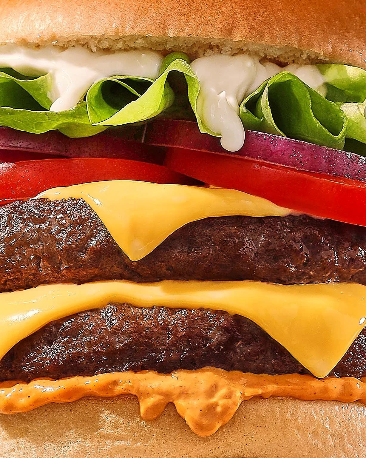 Food styling Gent. Close-up of a cheeseburger with lettuce, tomato, onions, cheddar cheese, and burger patties with sauce, all in a bun.