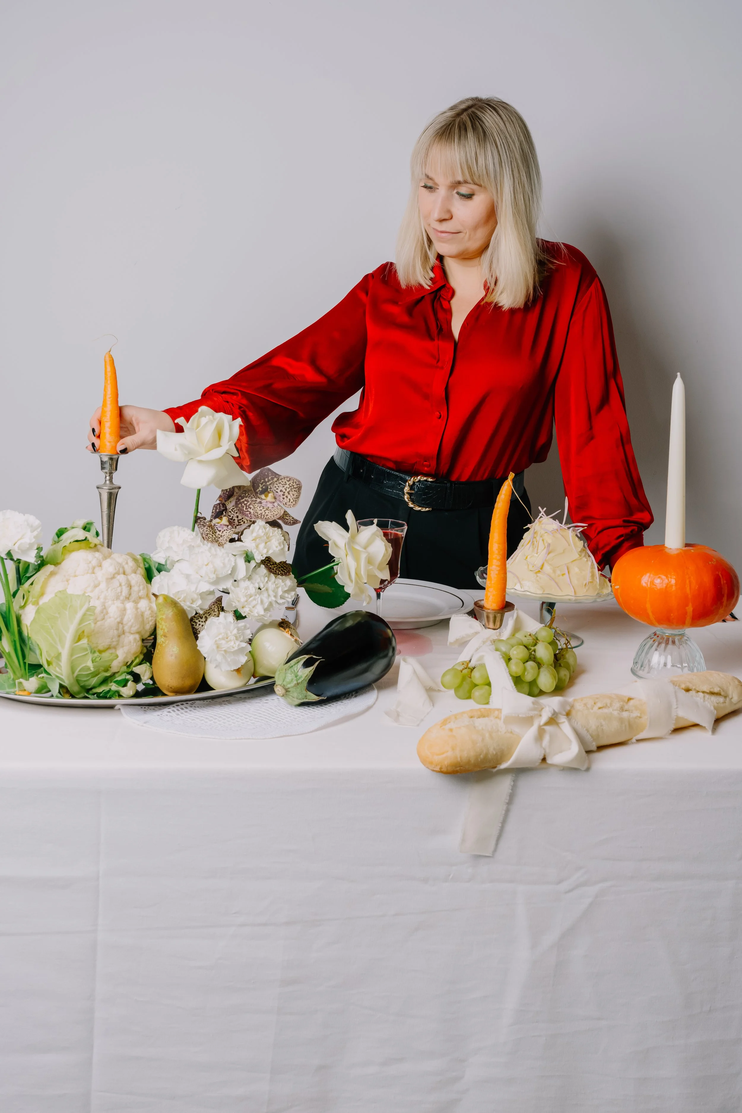 Sarah Ghijselinck, food and drink stylist, Gent, Woman arranging a table with vegetables, flowers, candles, and bread for a celebration or dinner.