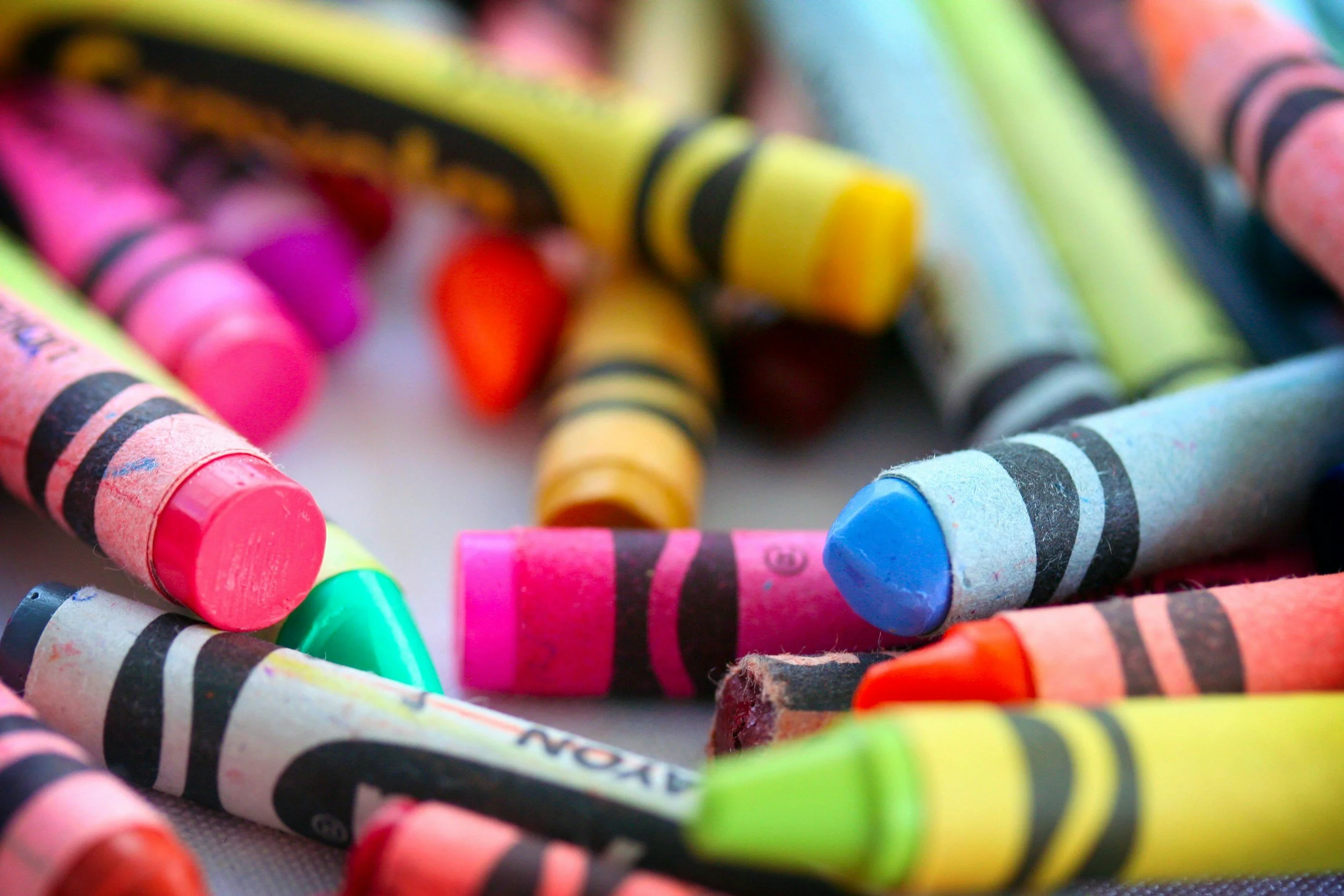 Close-up of a pile of colorful crayons, including pink, yellow, blue, green, and orange.