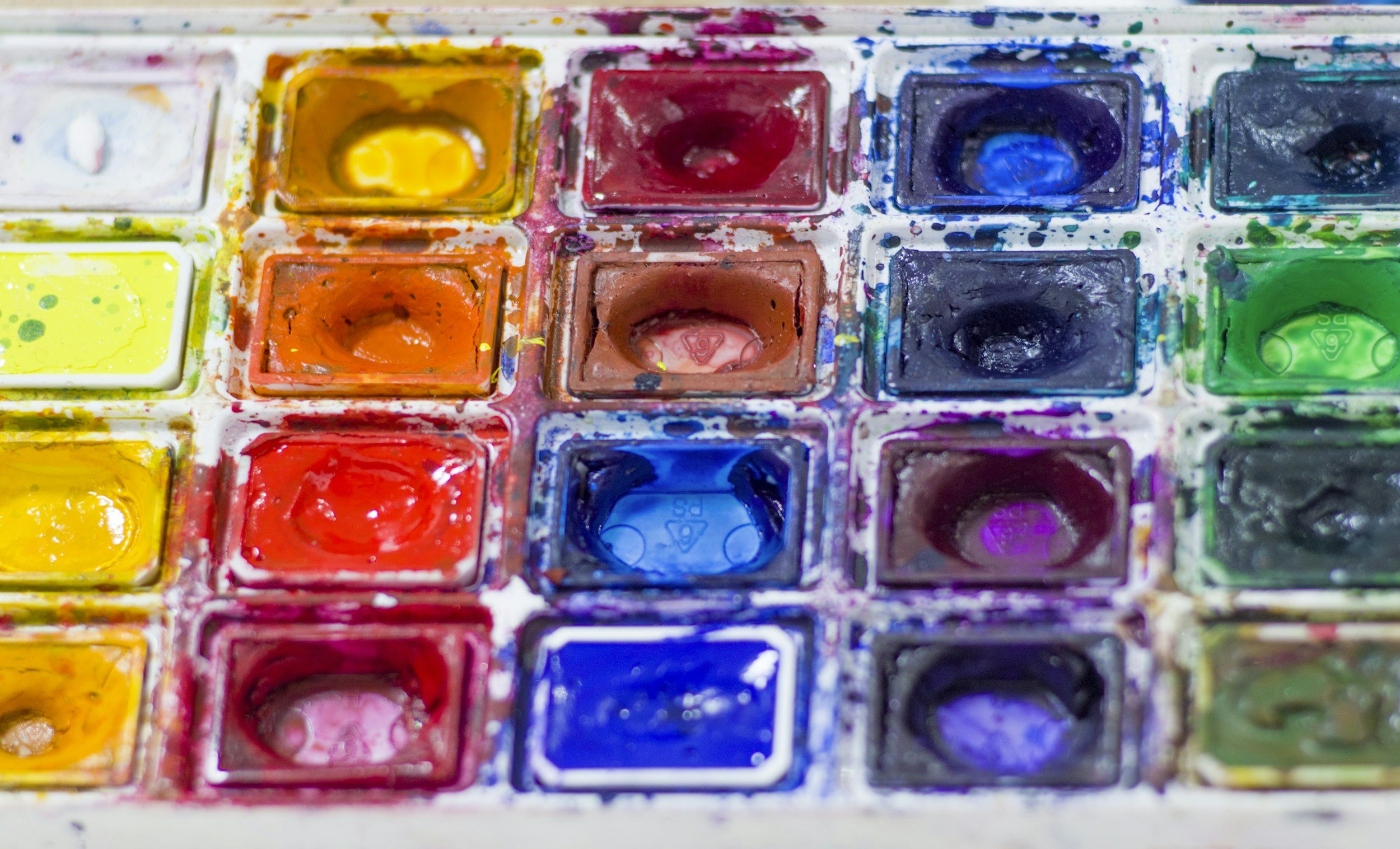 Close-up of watercolor paint palette with various colors, including yellow, orange, red, blue, black, and green.