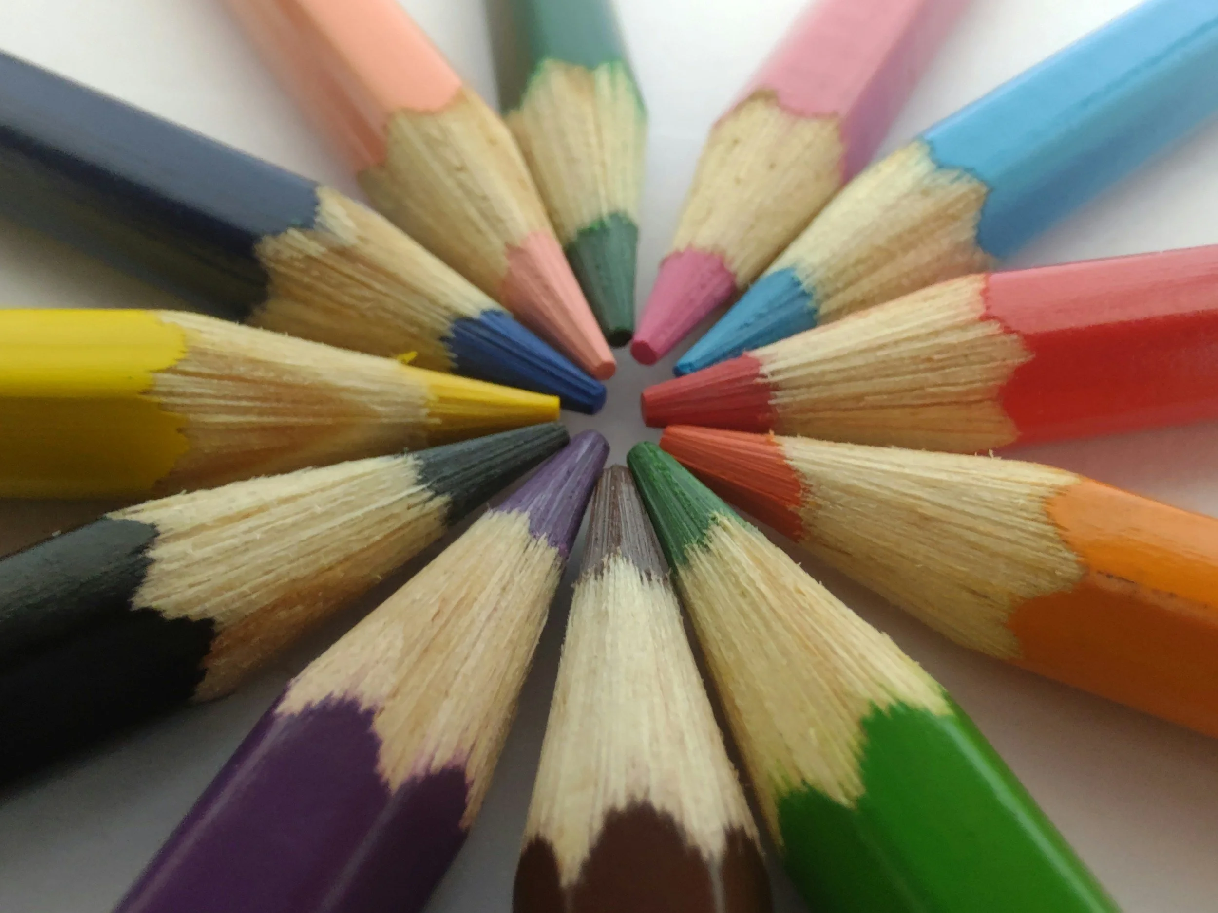 Close-up of sharpened colored pencils arranged in a circle with the points facing inward, displaying various colors.