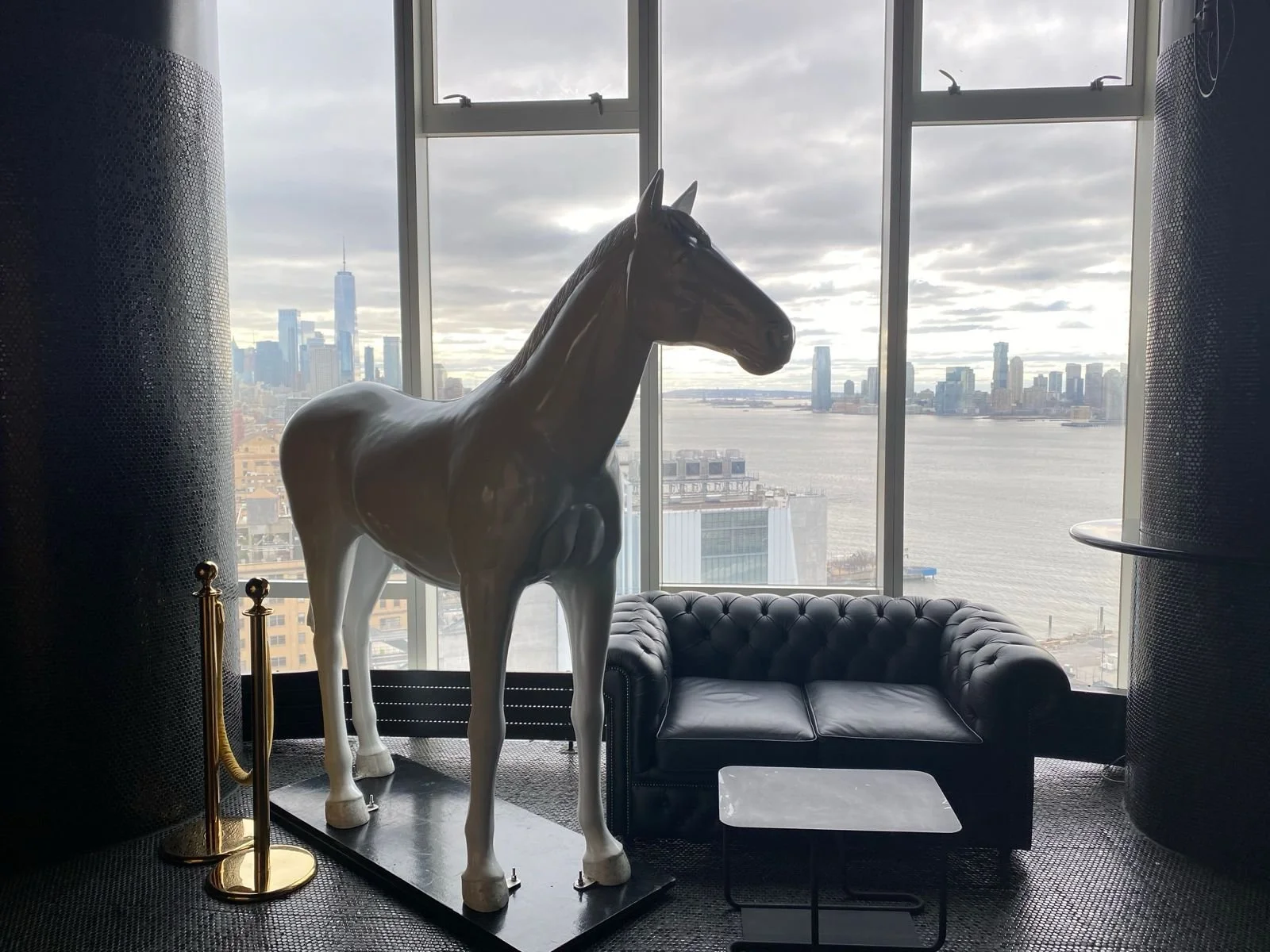 A custom two seater leather sofa in a New York rooftop in front of a view of the city and a real size horse statue