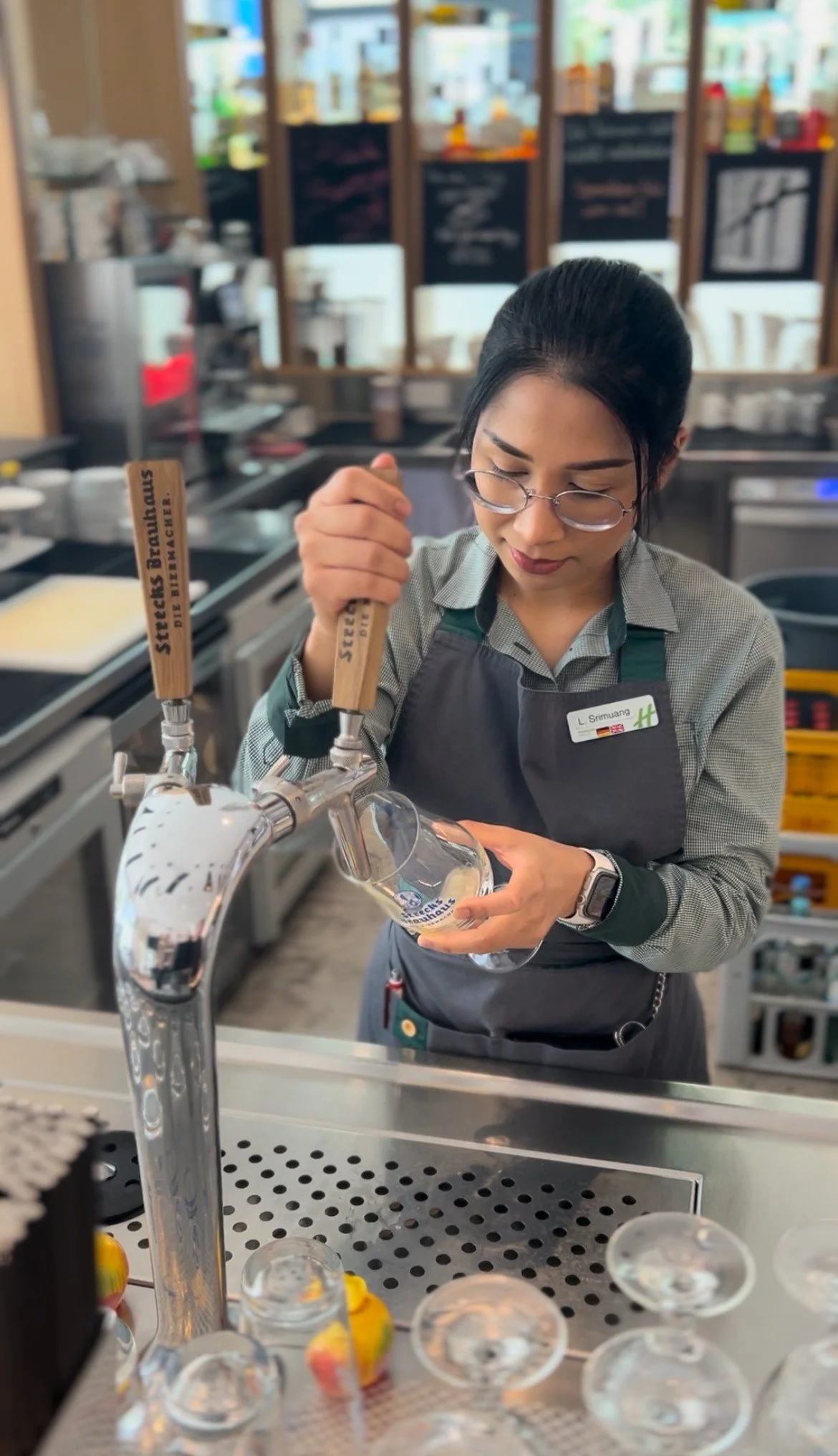 A woman pouring beer from a tap into a glass at a bar or brewery.
