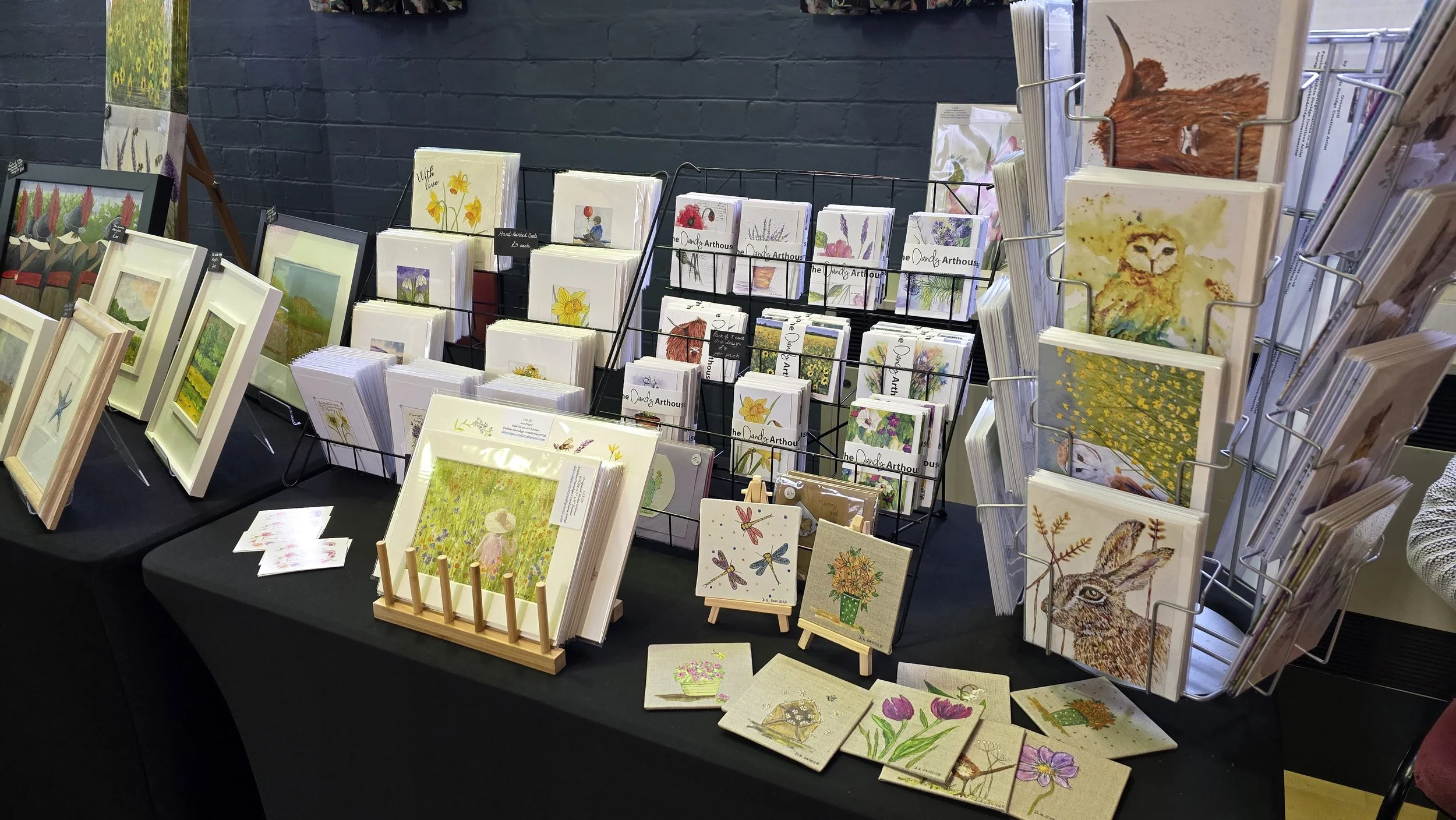 Display of various watercolor art prints and greeting cards featuring animals, flowers, and nature themes arranged on tables and wire racks.