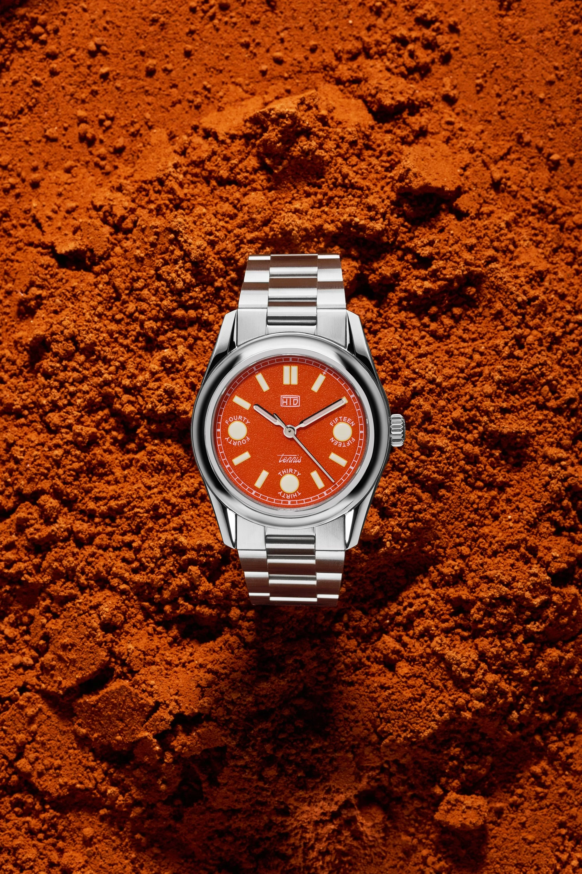 Still life dell’orologio HTD Watches Tennis Terra Rossa su terra rossa, in un richiamo diretto all’estetica dei campi da tennis