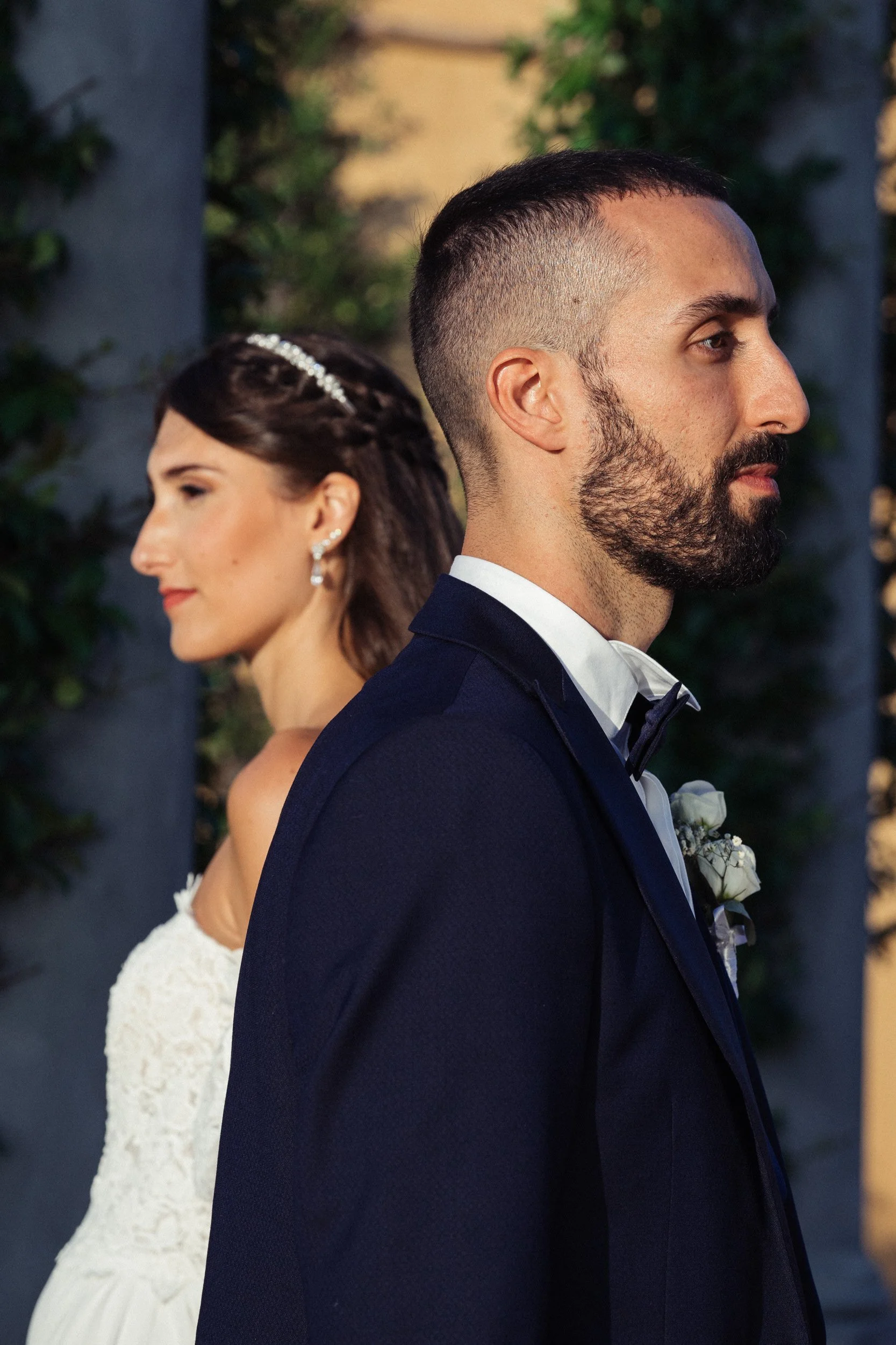 Una coppia di sposi in abiti formali, con sfondo di vegetazione e luci soffuse.