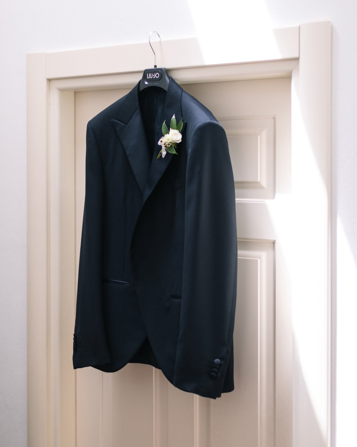 Un completo da uomo nero con fiorellini sull'appendiabiti appeso a una porta bianca.