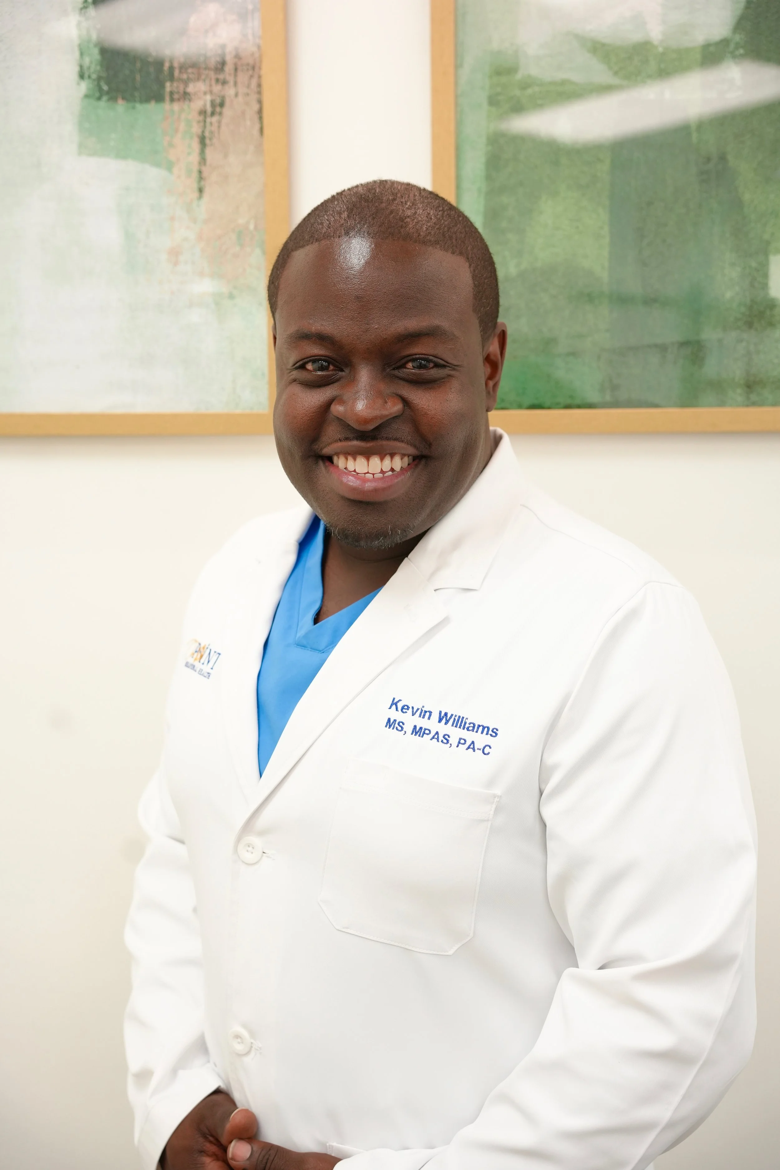 A smiling man in a white medical coat standing in front of abstract artwork.