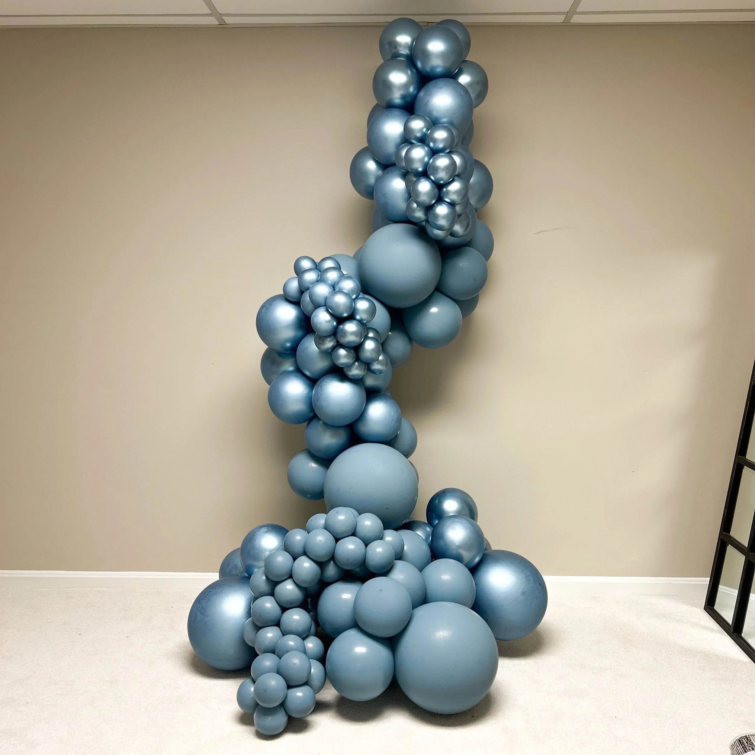 Blue metallic balloon display with various sizes of balloons arranged in a cascading pattern against a beige wall in Cleveland, Northeast Ohio.