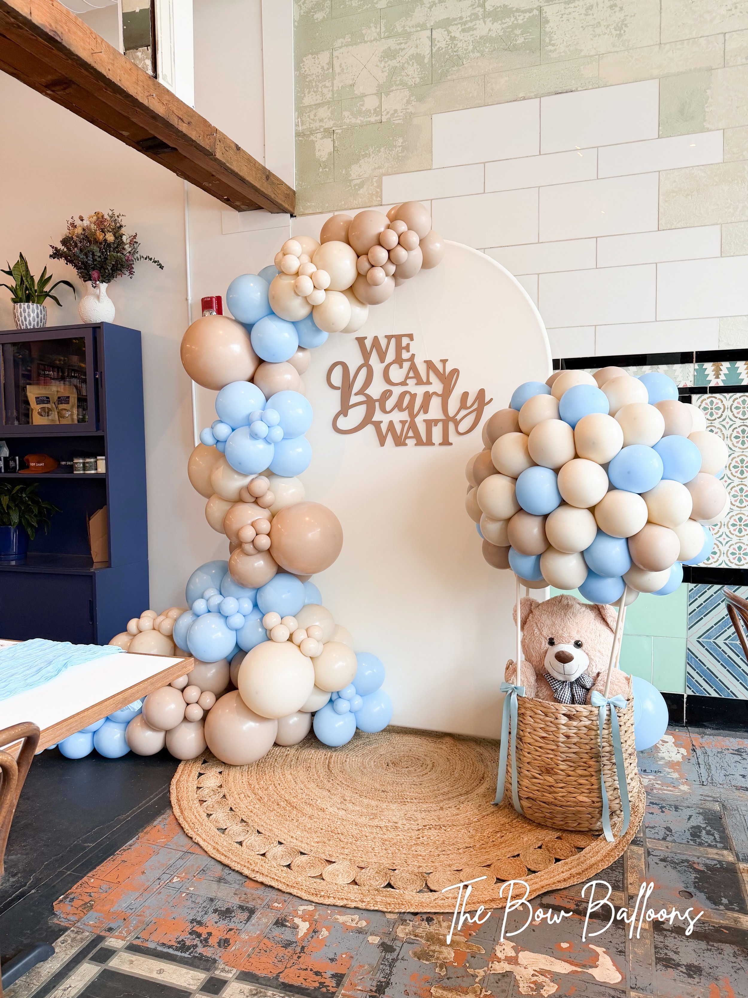 Baby shower balloon decor featuring a teddy bear hot air balloon, decorative balloon garland, and a whimsical themed backdrop.