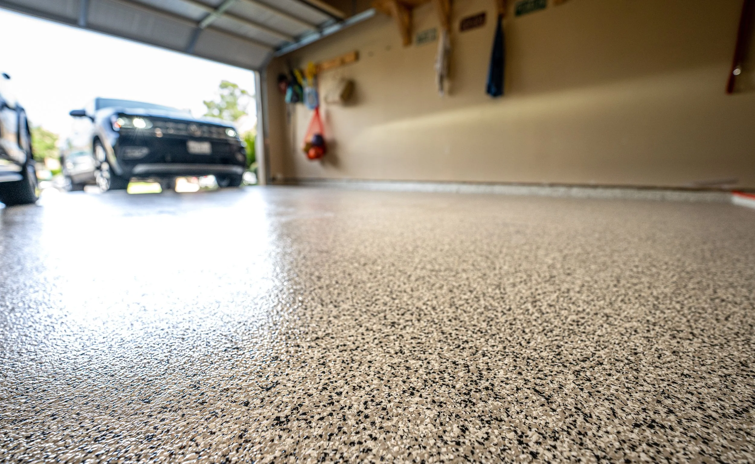 Close-up view of a textured garage floor with a parked car visible outside through the open garage door.