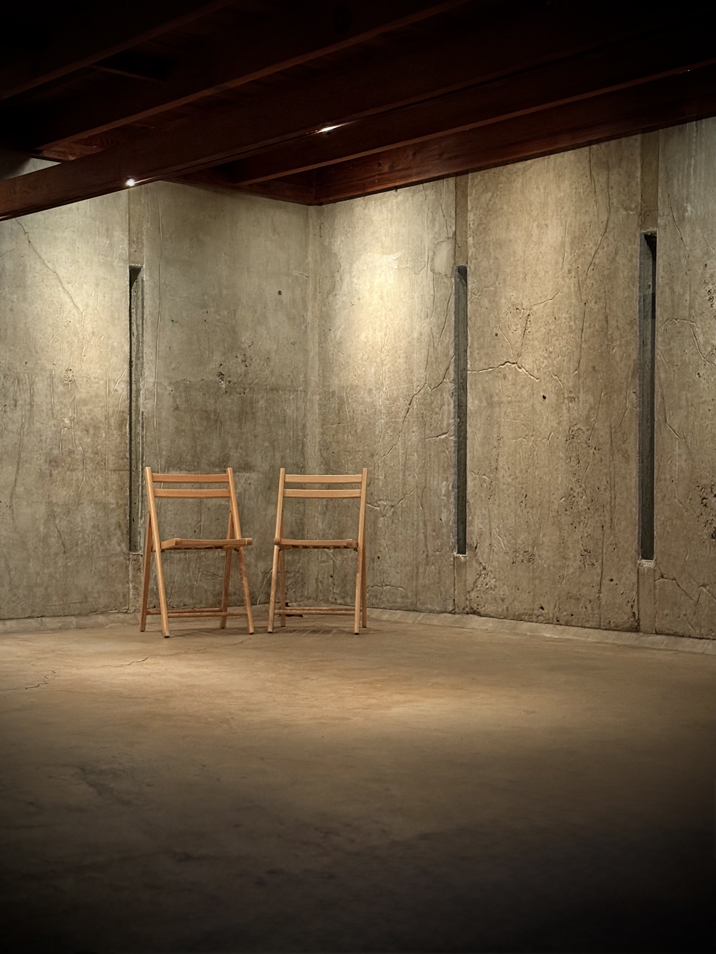 Two empty wooden chairs in empty open room with mood lighting.