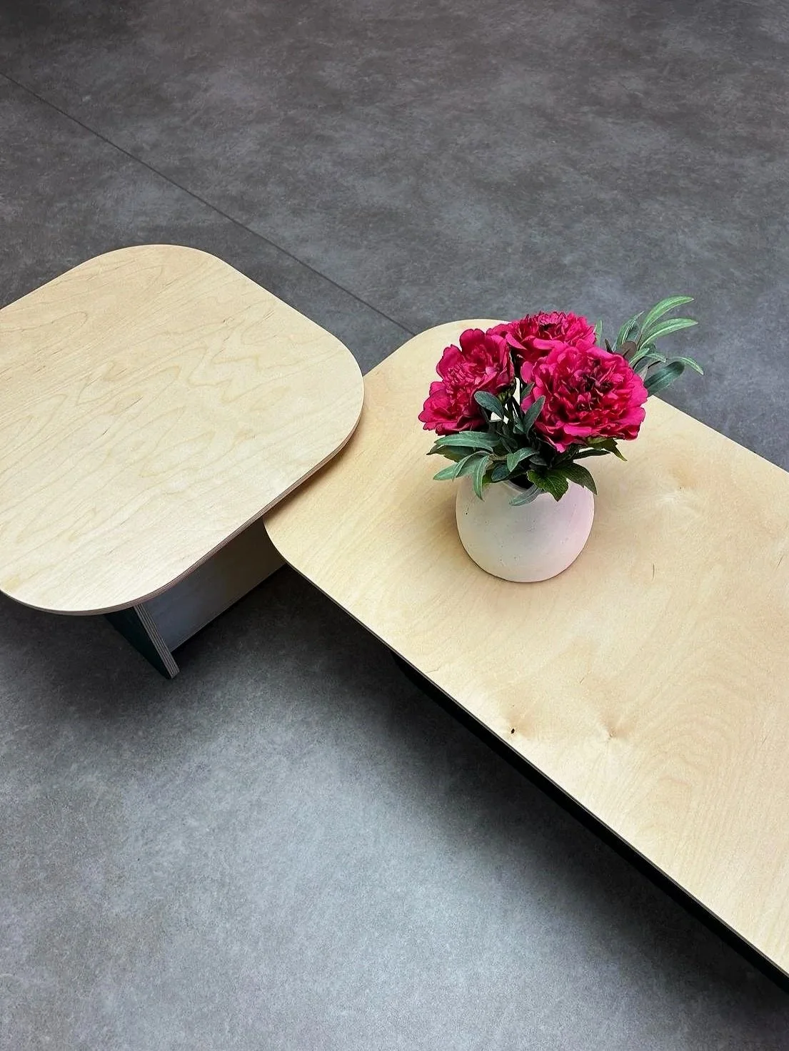 A custom light wood table with a minimalist white vase and fresh flowers, showcasing contemporary furniture design and natural materials.