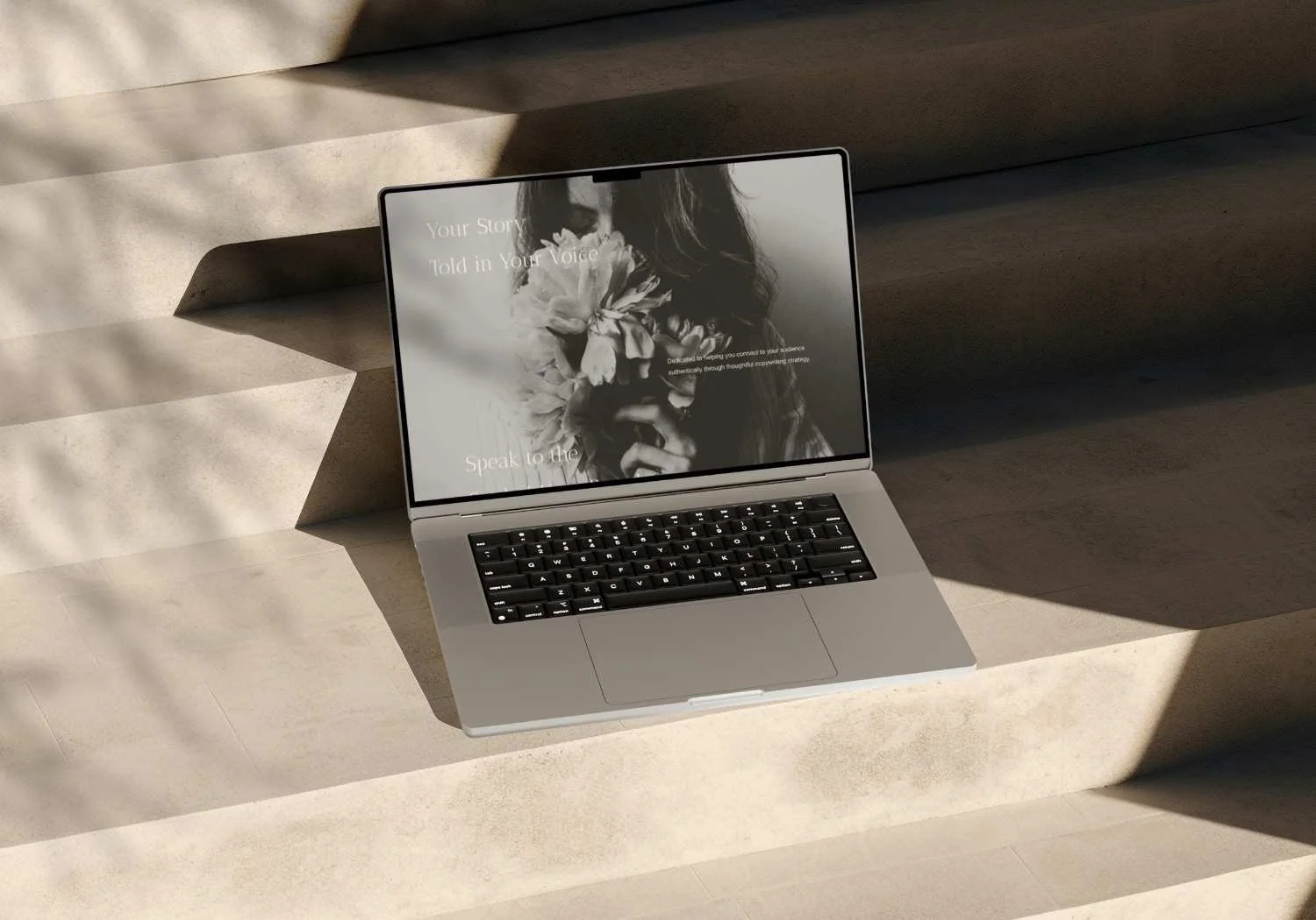 An open silver laptop on beige concrete stairs with sunlight casting shadows, screen displaying a grayscale image of the "Quill" Squarespace Template homepage featuring a woman holding flowers to her face with text overlay.