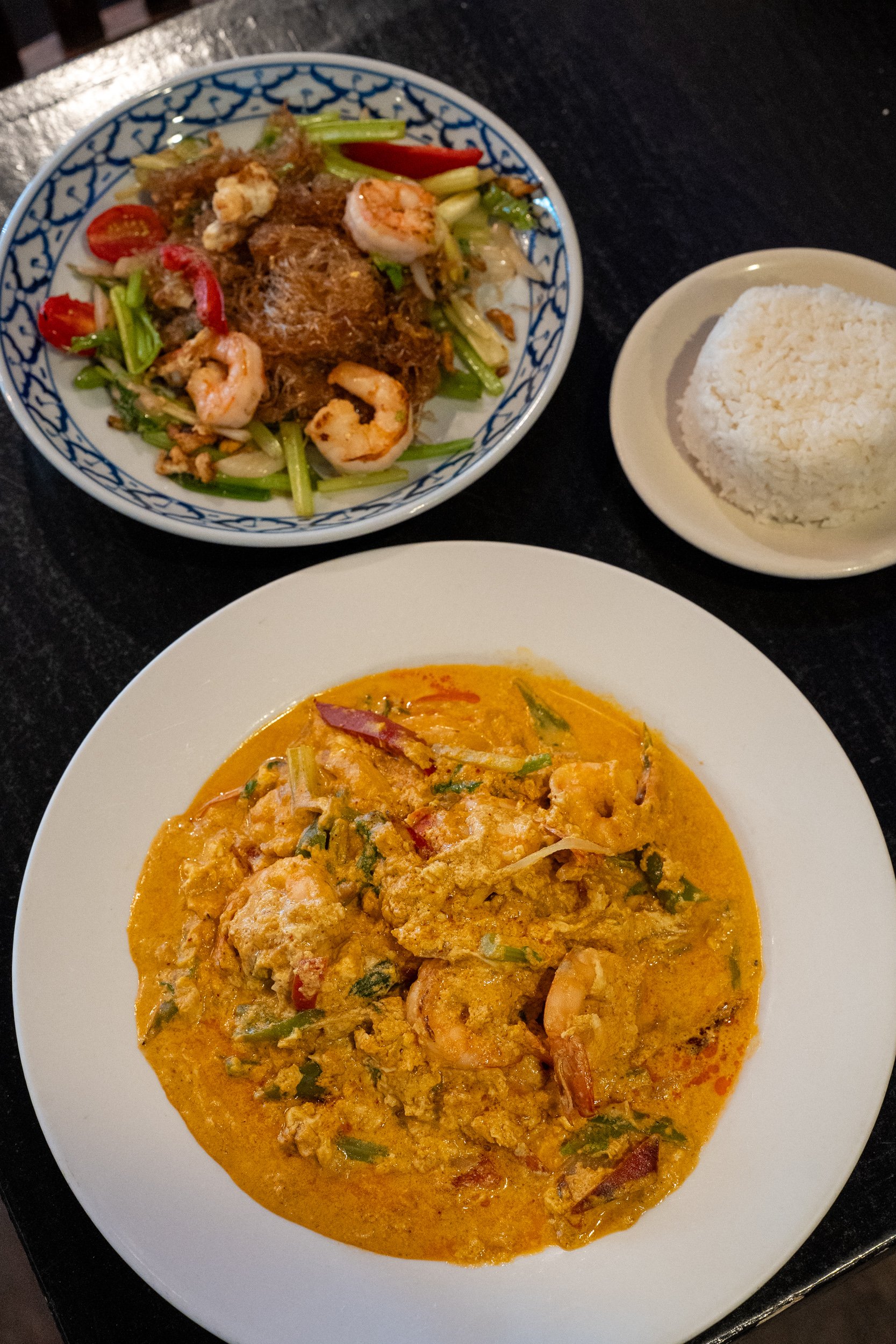 A plate of shrimp and curry with a bowl of rice and a side of vegetable salad.