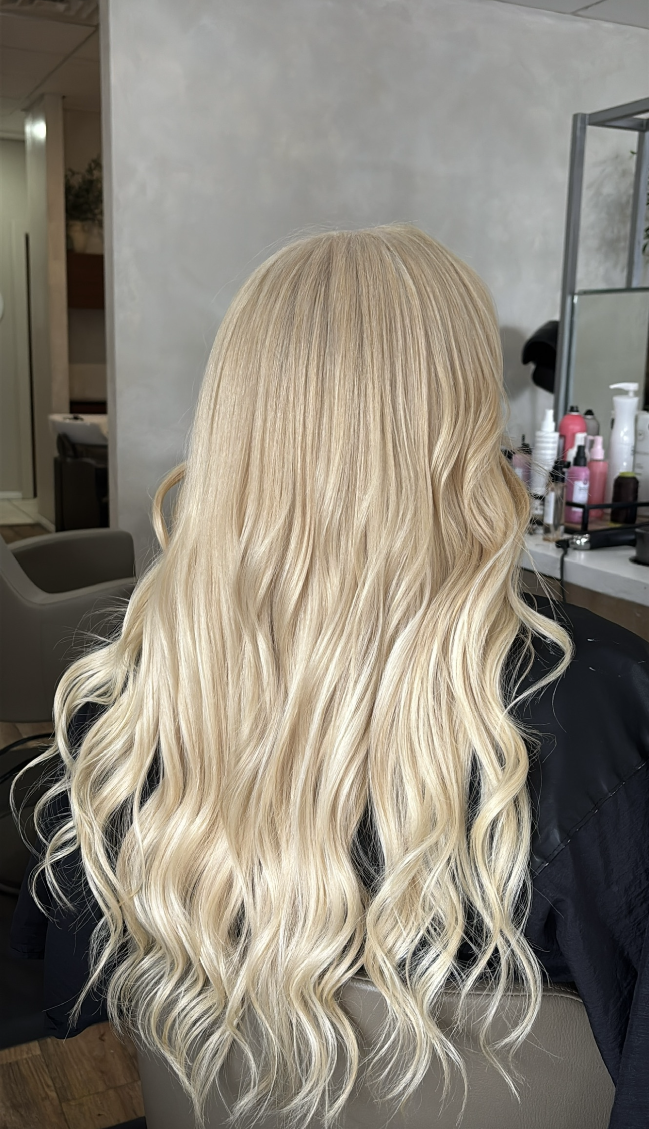 Long, wavy blonde hair flowing down the back of a person sitting in a salon chair.