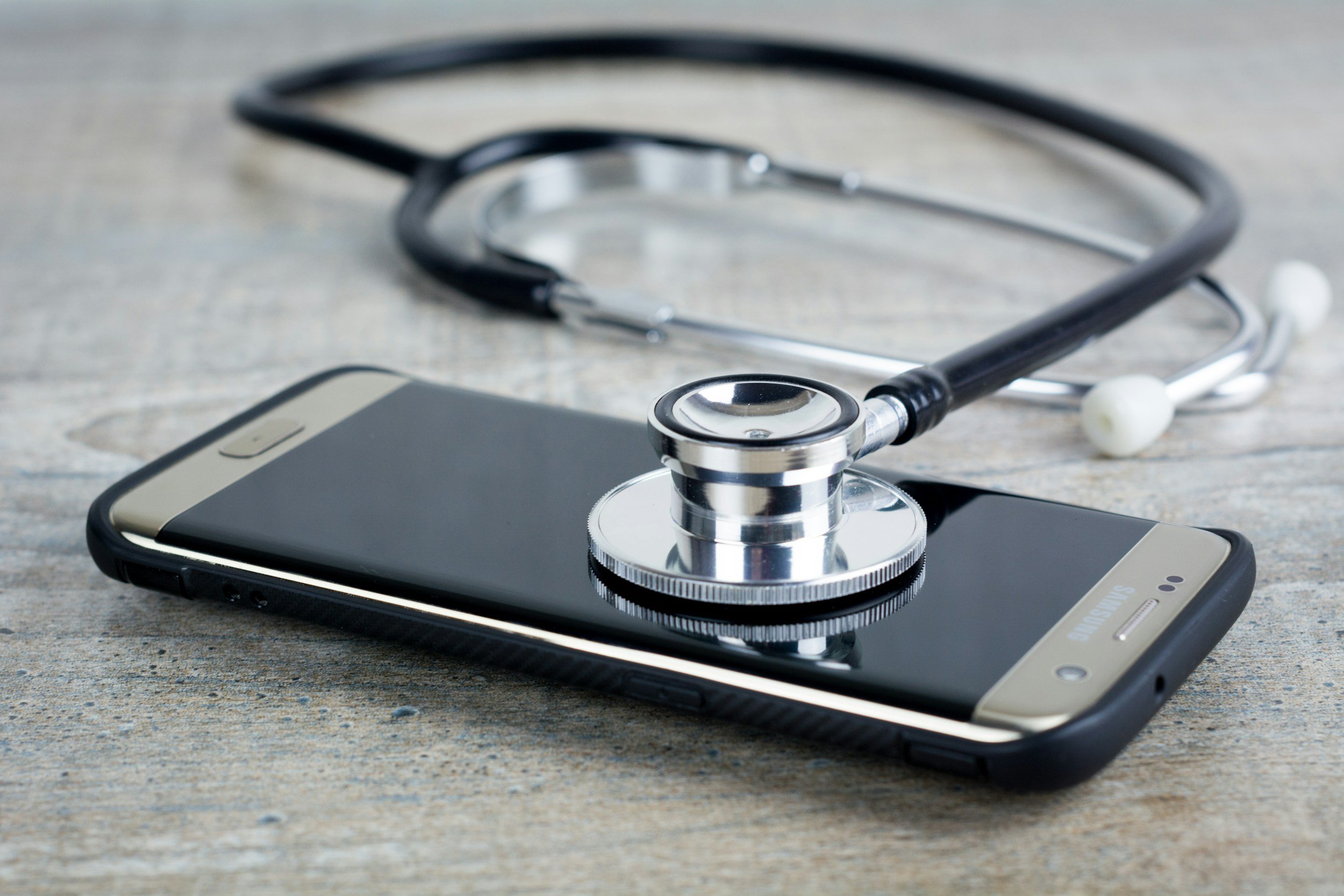 A stethoscope resting on a smartphone on a wooden surface.