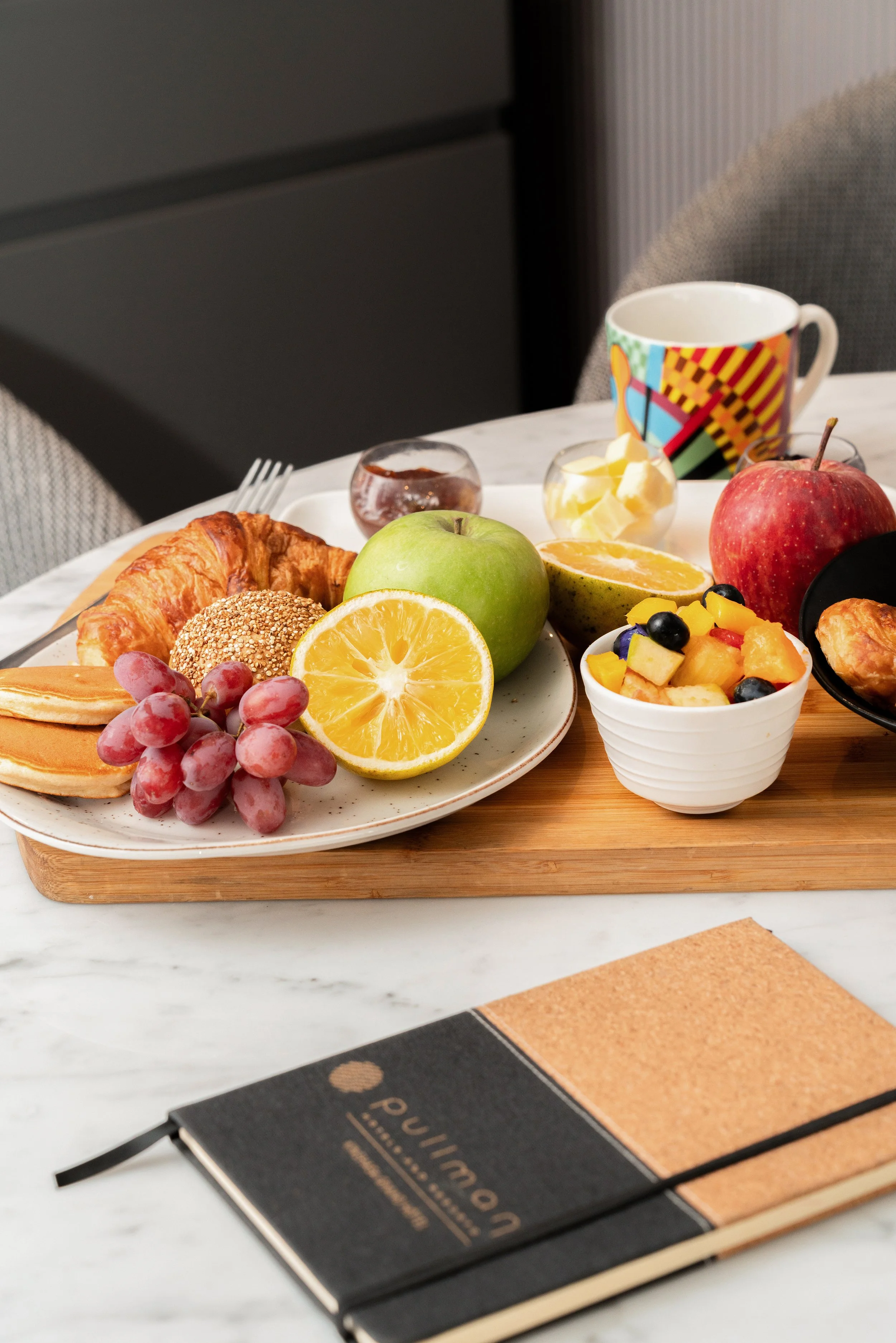 Petite table de petit-déjeuner avec fruits, croissants, pancakes, et une tasse colorée