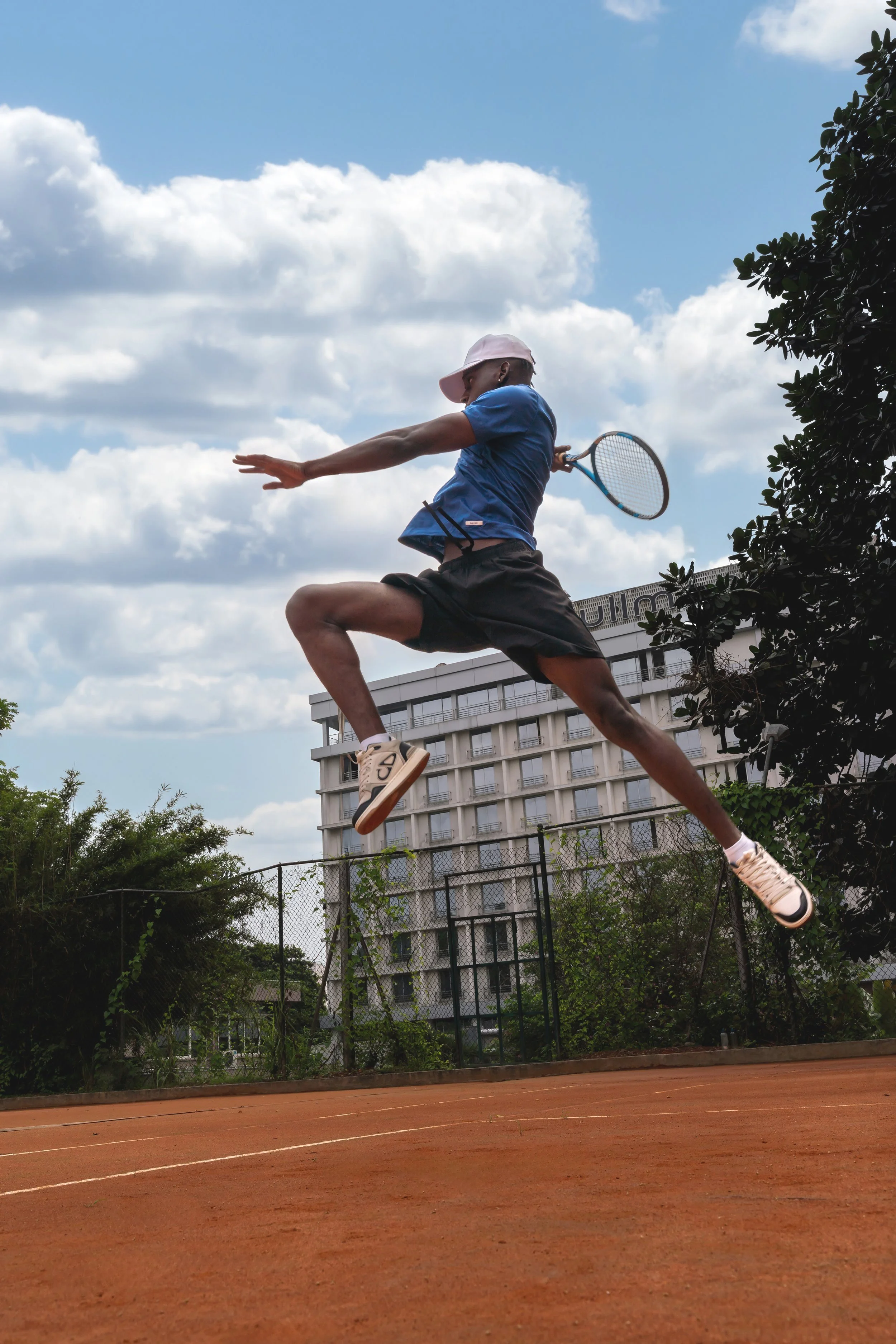 Un jeune homme joue au tennis sur un terrain en terre battue, en sautant dans les airs avec une raquette.