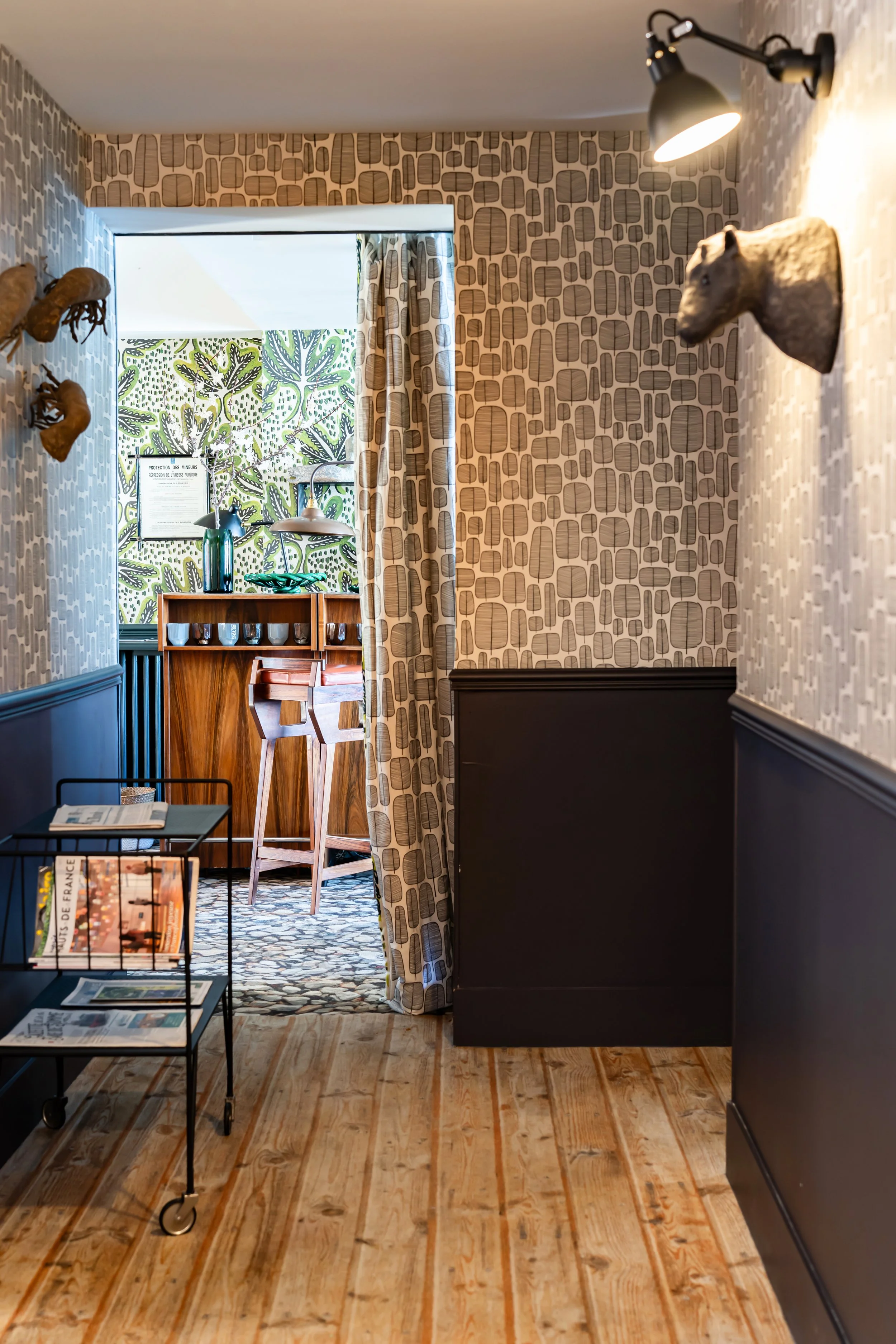 Intérieur d'une pièce avec murs décorés, un bar en bois avec des tabourets, et un décor avec des trophées d'animaux sur le mur.