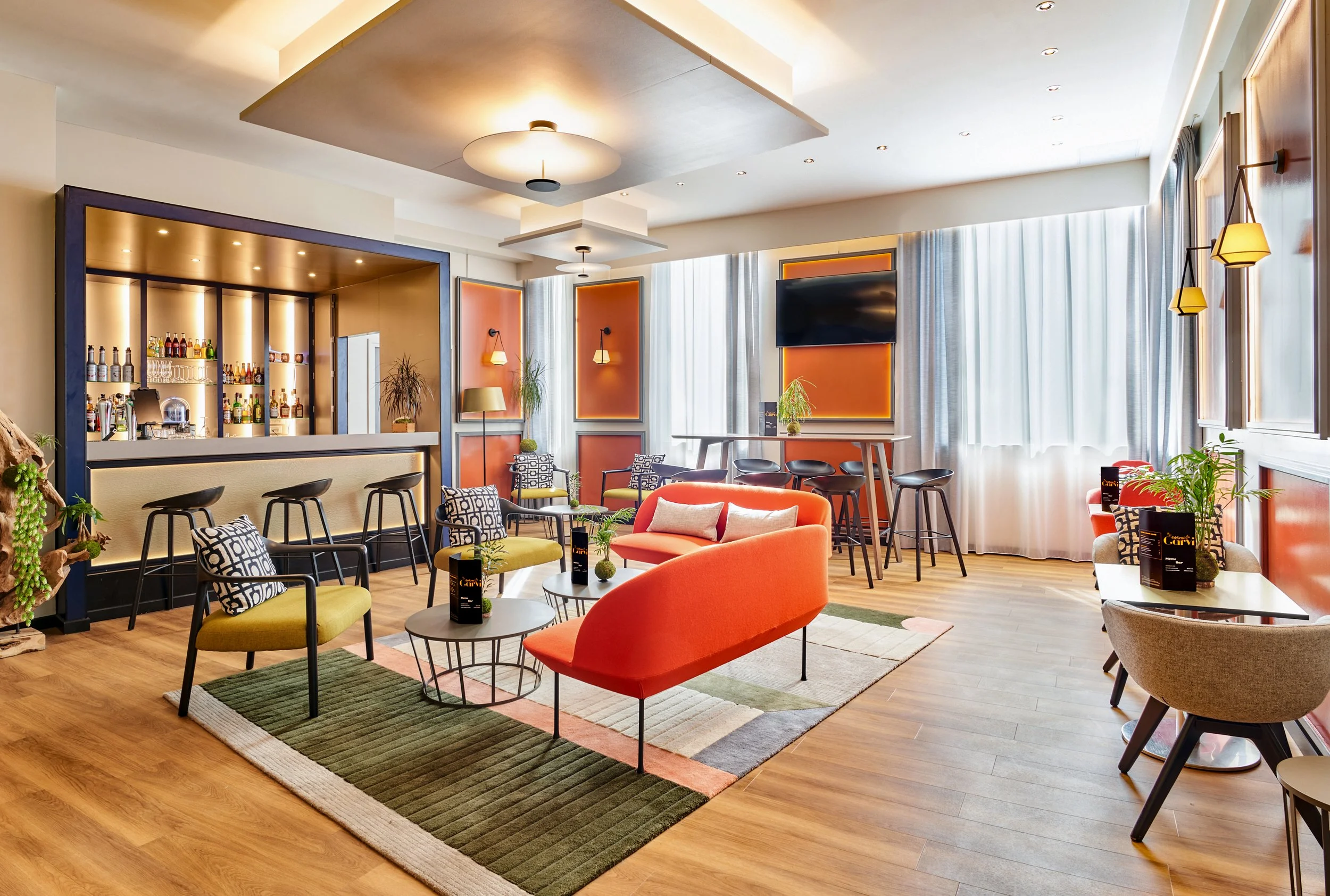 Salon moderne avec canapé orange, fauteuils verts et graphiques, bar avec tabourets, et grand écran TV, décoration colorée avec plantes et éclairages chaleureux.