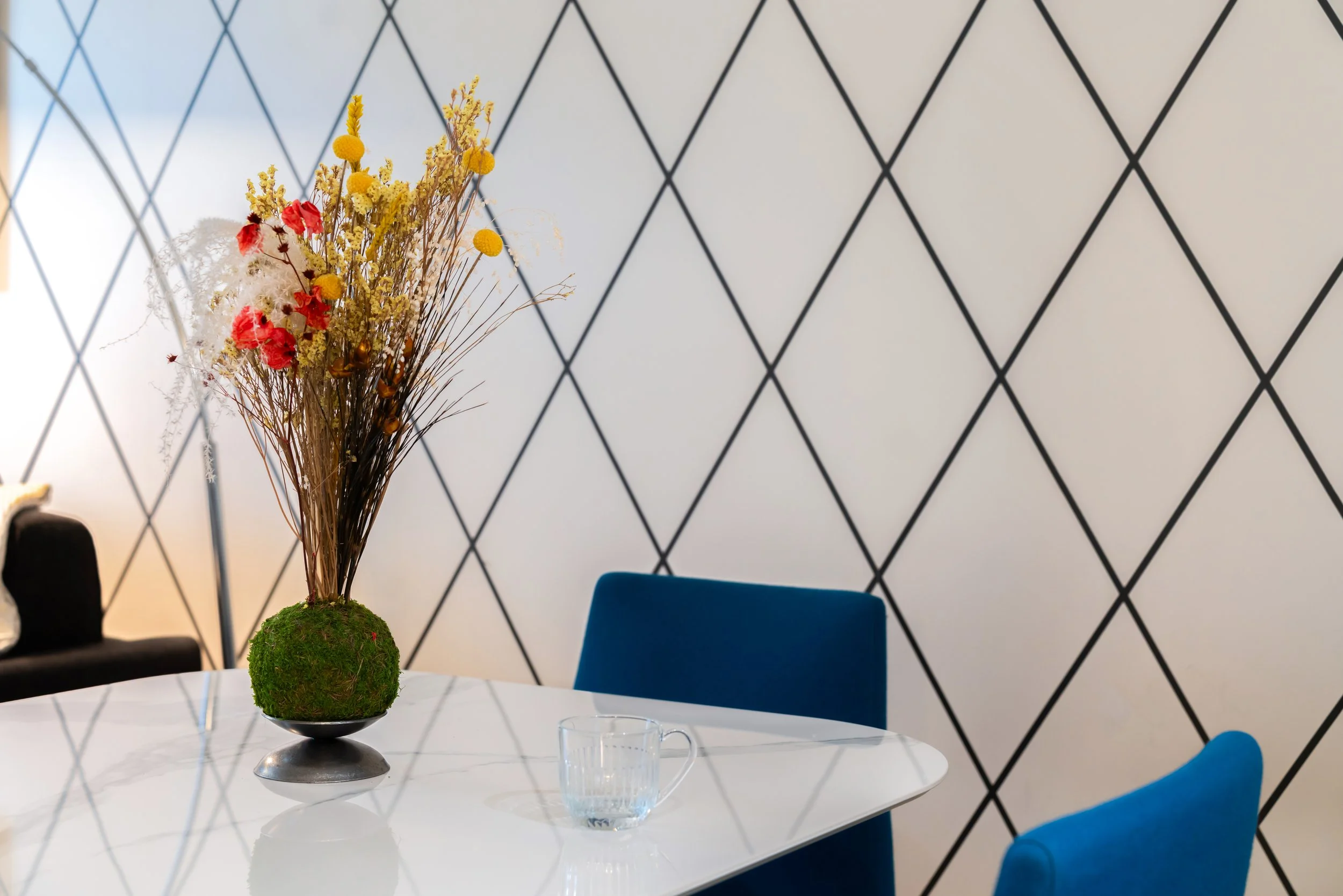 Vase avec bouquets de fleurs séchées sur une table blanche moderne avec un papier peint à motifs géométriques.