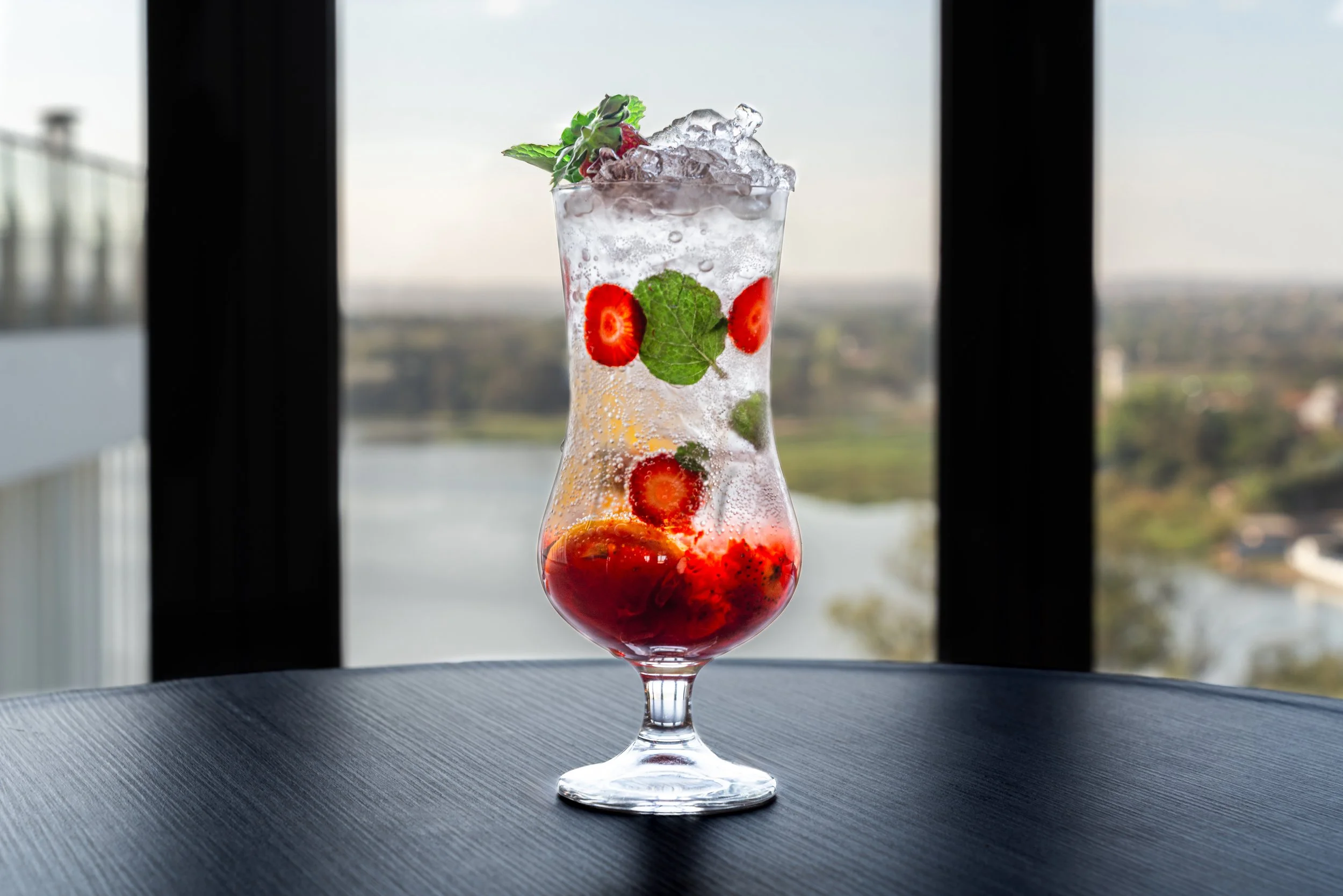 Cocktails avec des fraises, des feuilles de menthe et des glaçons, placé sur une table avec paysage flou en arrière-plan.