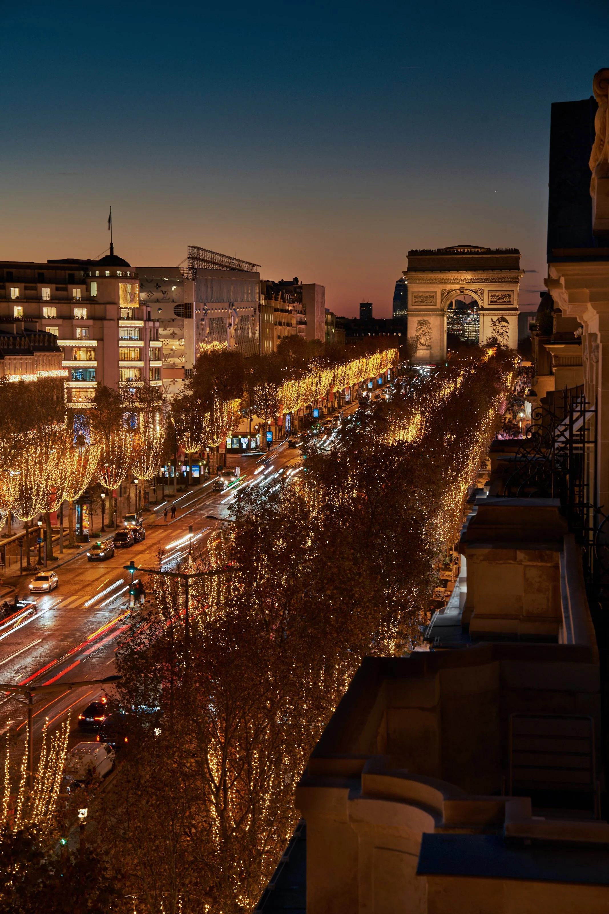 Vue nocturne de l'avenue des Champs-Élysées à Paris, illuminée de guirlandes lumineuses, avec l'Arc de Triomphe en arrière-plan.
