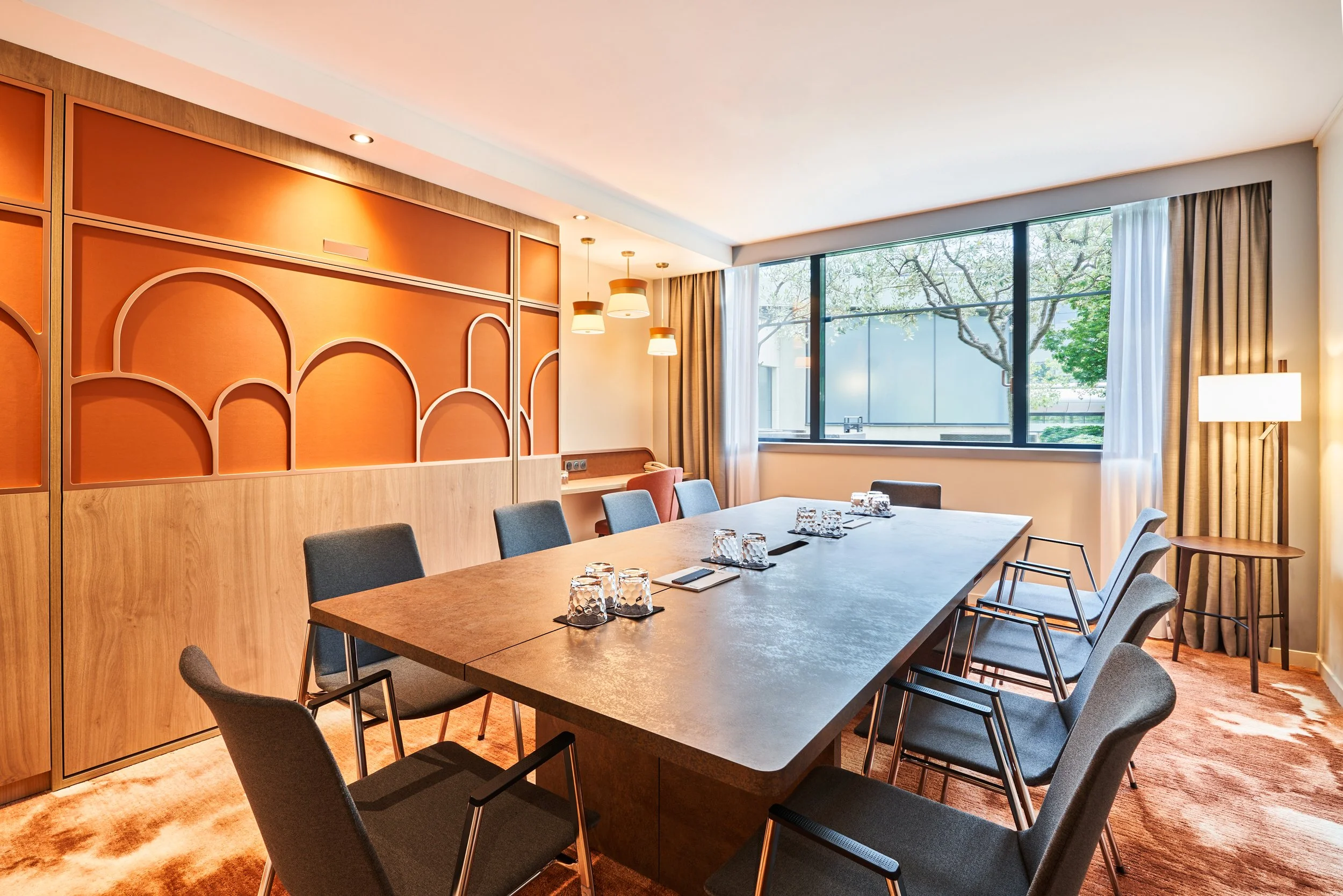 Salle de réunion avec table, chaises, grandes fenêtres et éclairage moderne.