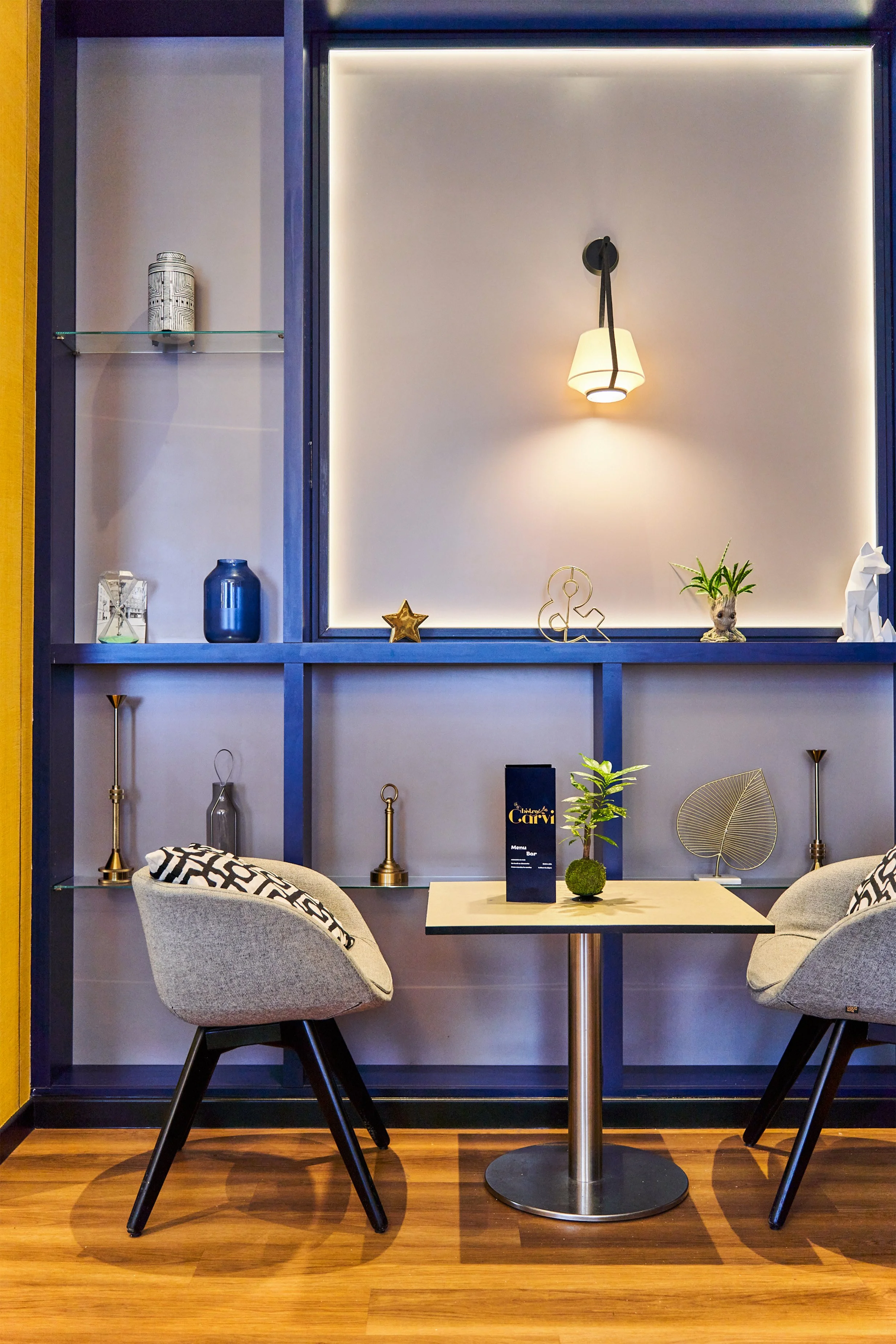 Intérieur d'un café avec deux chaises en face d'une table, décorations modernes sur une étagère derrière, éclairage ambiant doux.