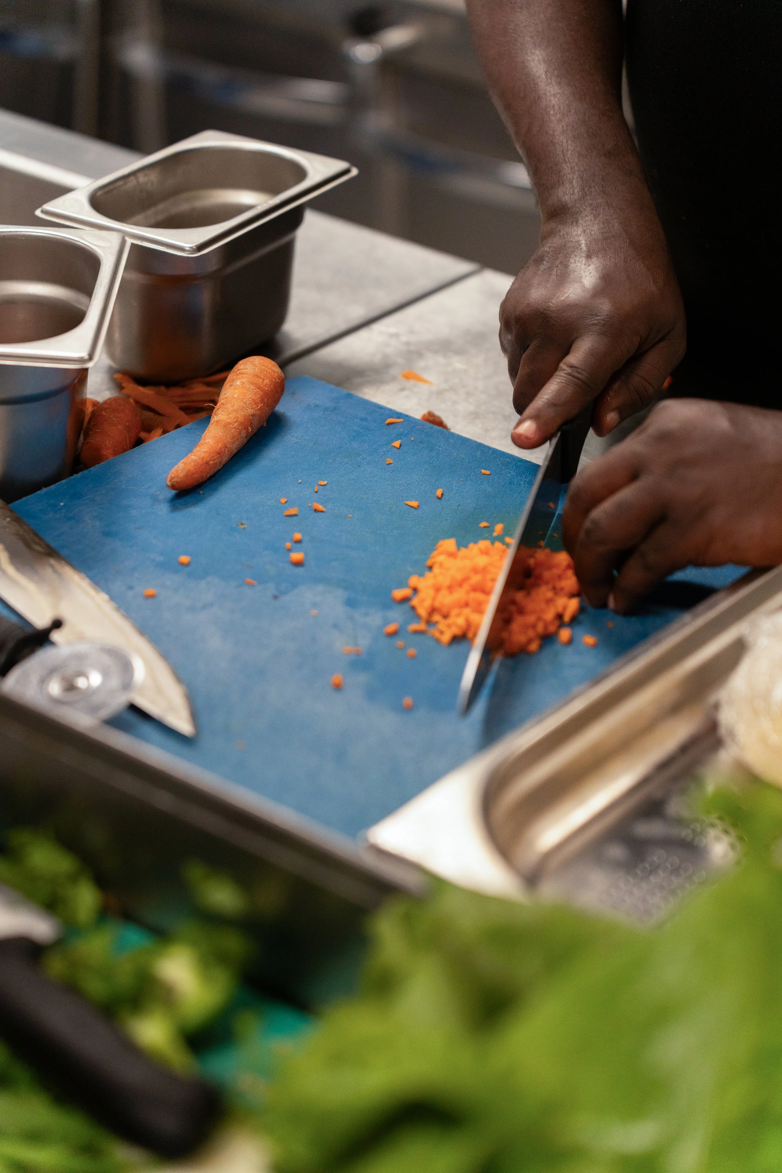 Une personne coupe une carotte en petits morceaux sur une planche à découper bleue dans une cuisine.